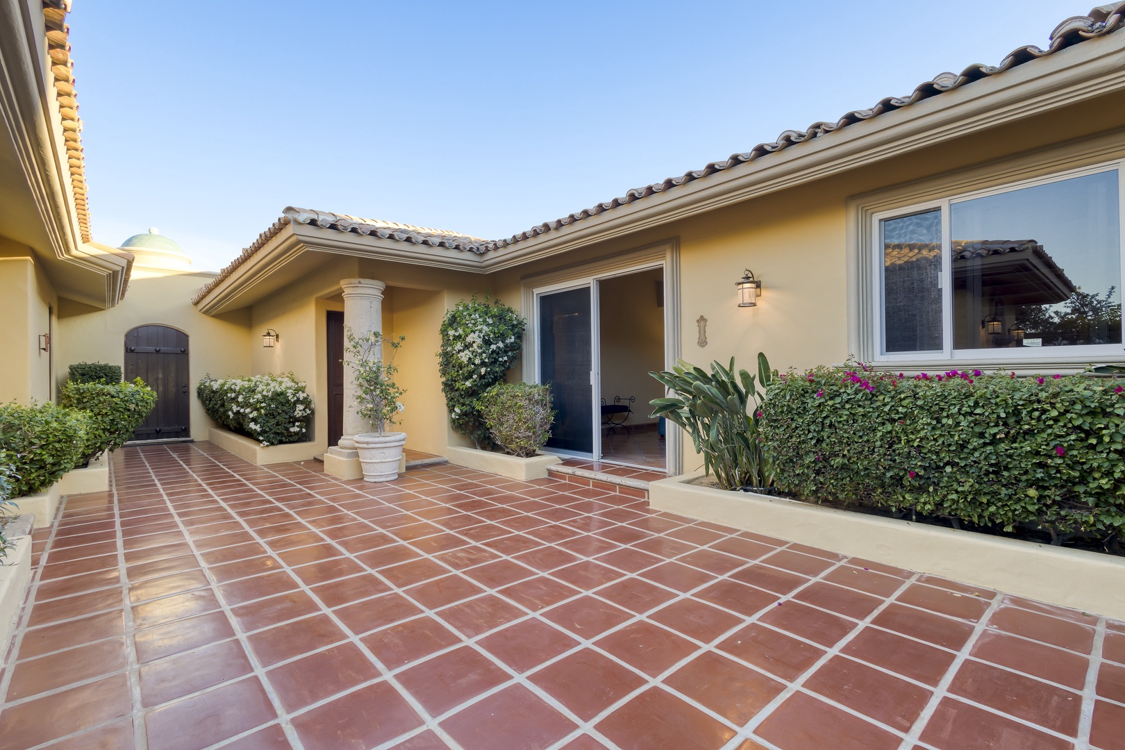 Mediterranean-style villa entrance featuring beautiful terra cotta tile flooring and lush landscaping surrounding the welcoming front entrance.