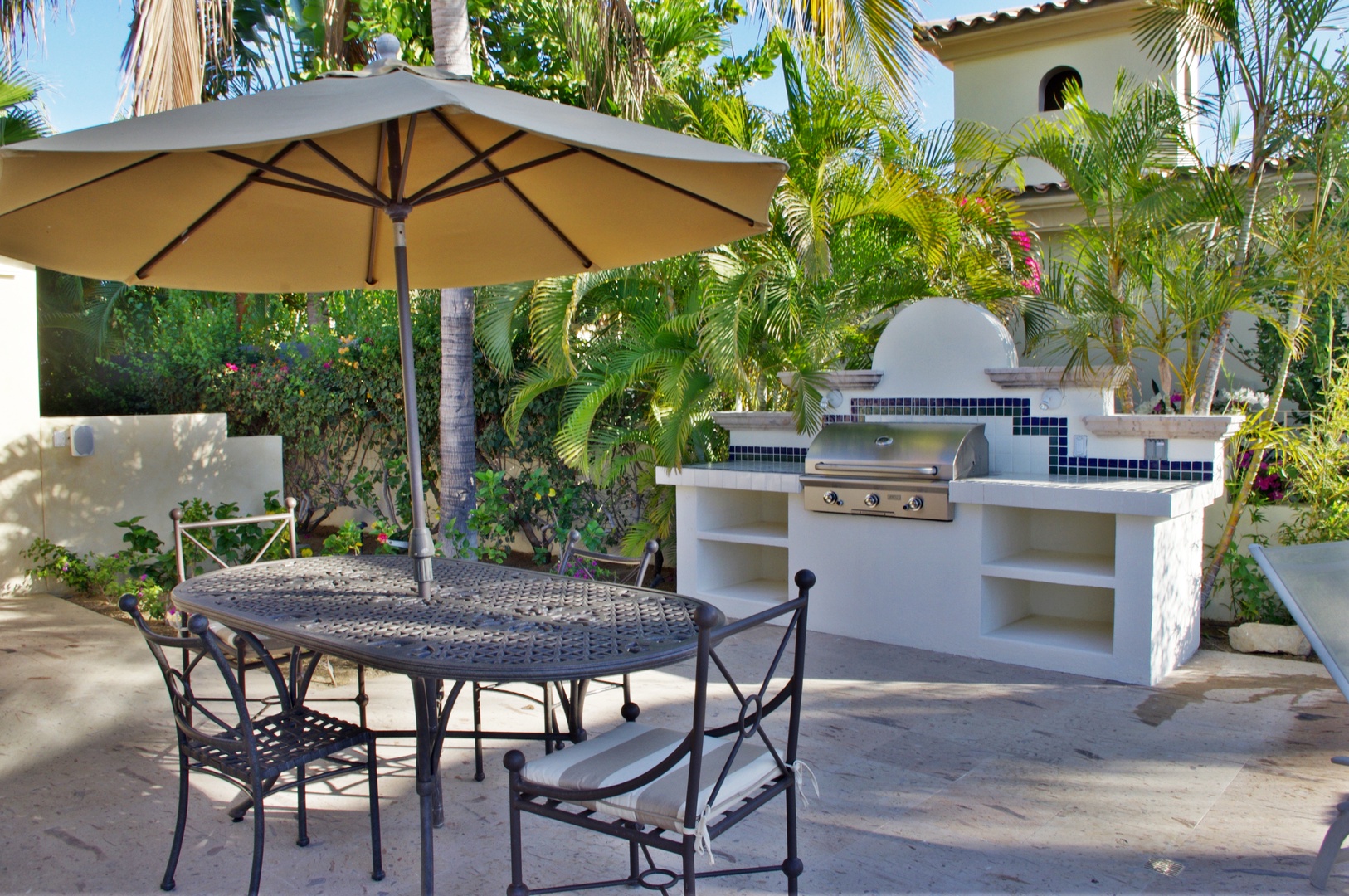 Your private outdoor kitchen awaits, complete with a built-in grill and shaded dining area surrounded by lush tropical palms—perfect for alfresco meals in paradise.