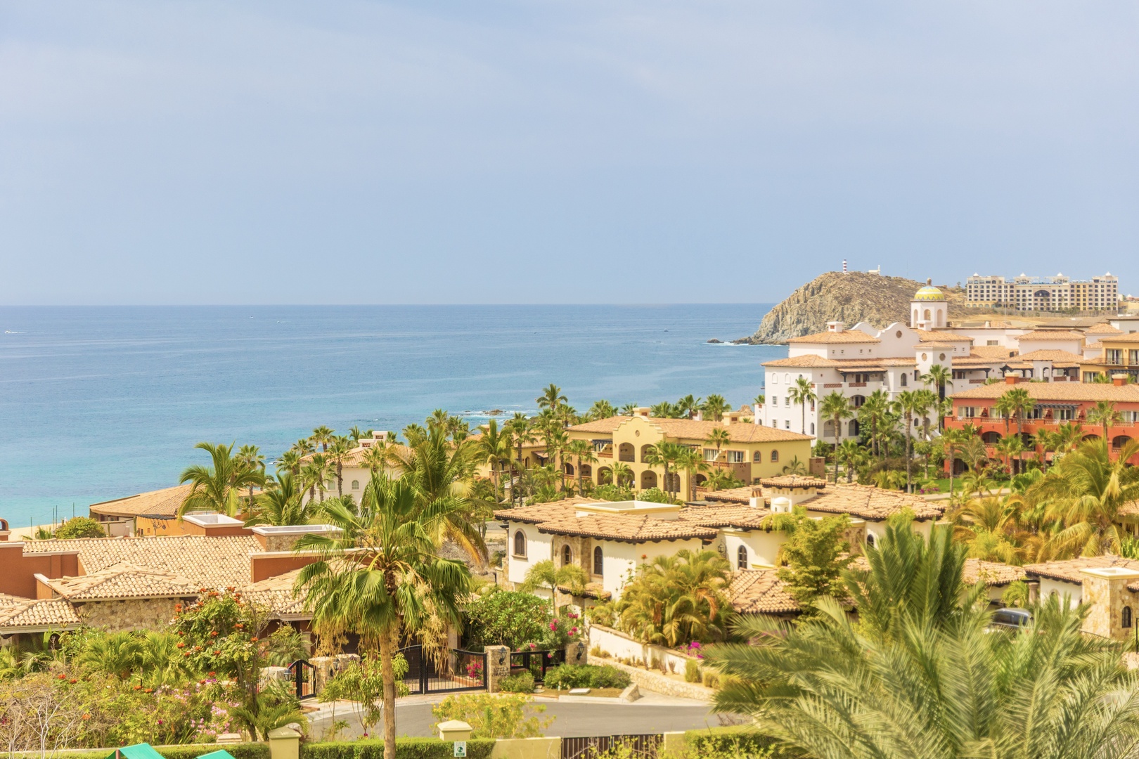 Coastal resort community features Mediterranean-style villas, palm trees, and pristine turquoise waters stretching to the horizon.