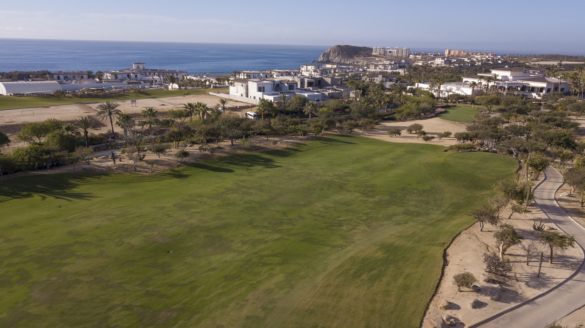 Championship golf course with pristine fairways stretches toward the azure coastline, creating an idyllic setting for recreational activities.