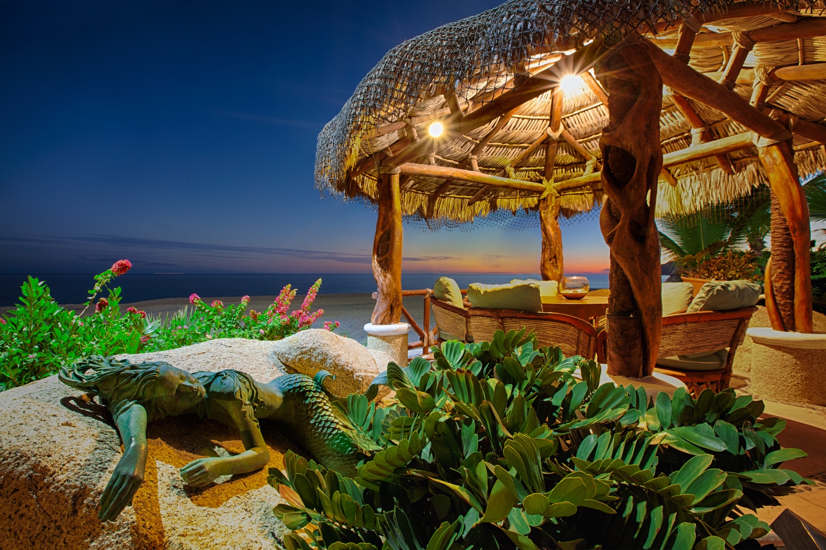 Oceanfront palapa terrace with tropical landscaping and comfortable seating area overlooking the sea at twilight.