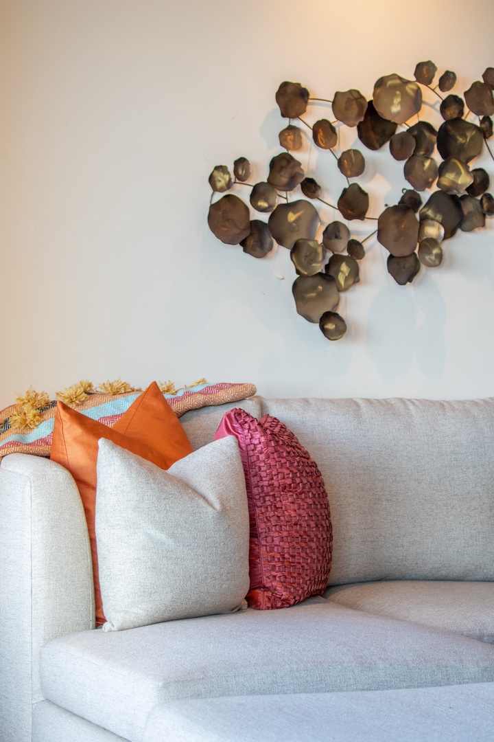 Sink into this inviting sofa adorned with vibrant pillows, where warm tones and artistic metal wall decor create your perfect retreat for relaxation.