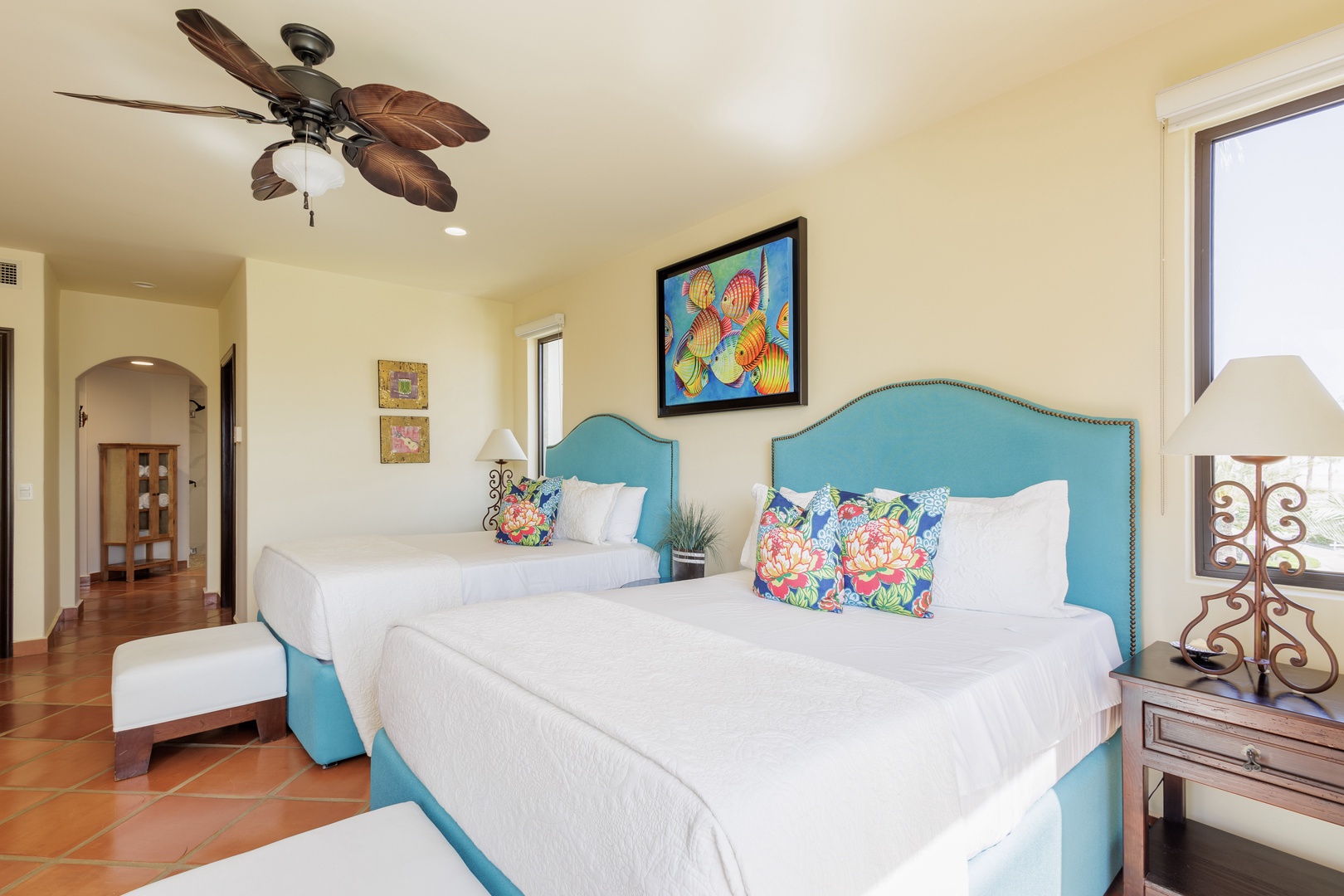 Your bright, cheerful bedroom awaits with two plush beds dressed in crisp linens and vibrant tropical pillows. Relax under the ceiling fan as natural light fills the space.