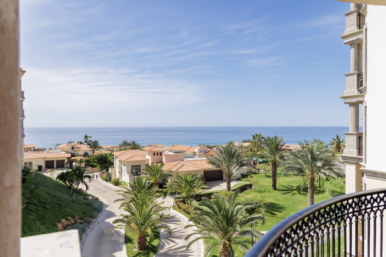 The property overlooks a landscaped resort community with Mediterranean-style villas and palm-lined grounds, with the sea visible in the distance beyond the coastal neighborhood.