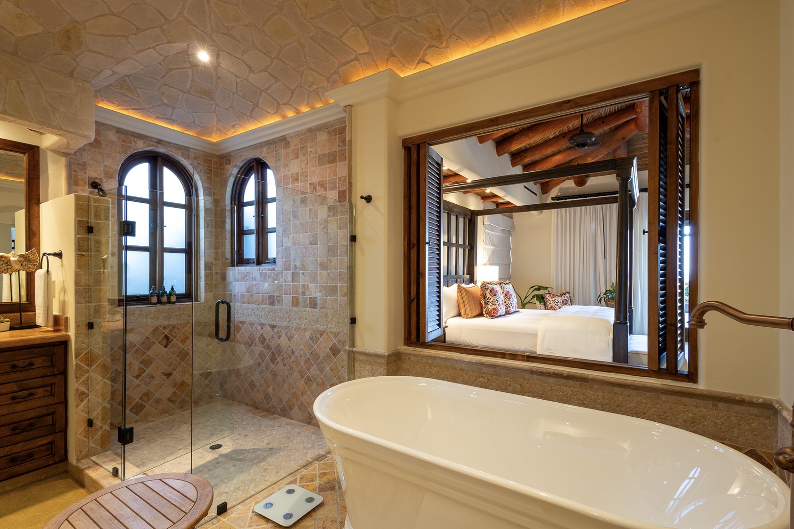 Your private spa-like bathroom features a soaking tub, glass-enclosed shower with elegant arched windows, and opens to your inviting bedroom. Warm lighting and handcrafted details create the perfect retreat.