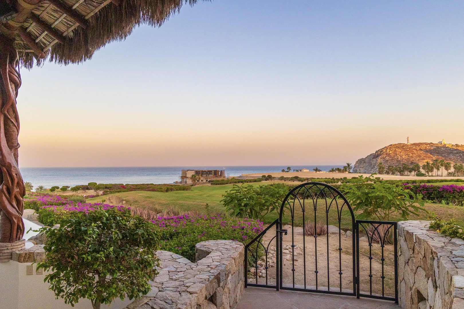 Sweeping coastal views unfold before your private terrace, where vibrant bougainvillea frames manicured gardens, distant hillsides, and tranquil sea horizons bathed in warm sunset light.