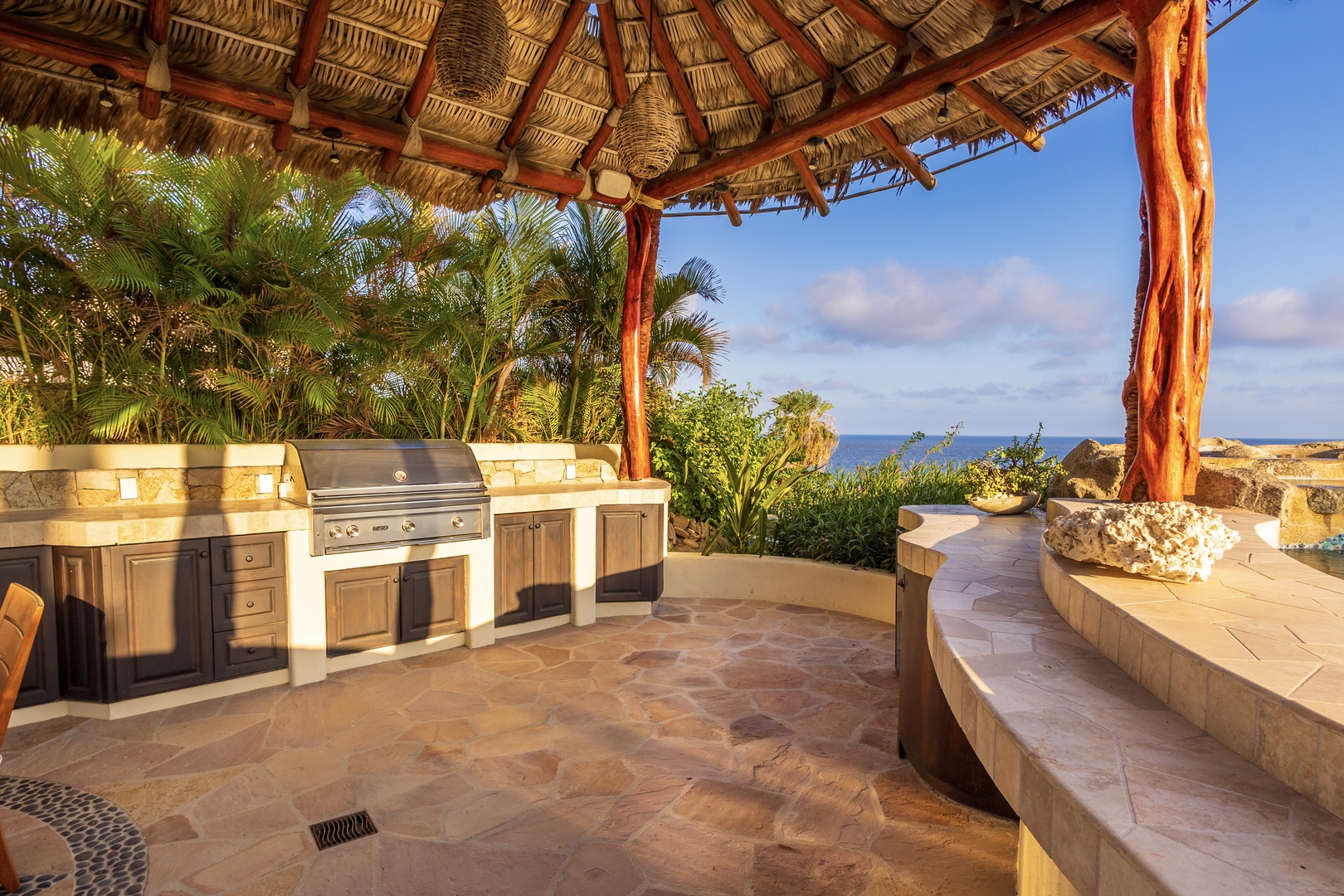 A thatched-roof palapa frames an outdoor cooking area with a built-in grill, counter space, and stunning sea views—perfect for grilling fresh meals in tropical paradise.