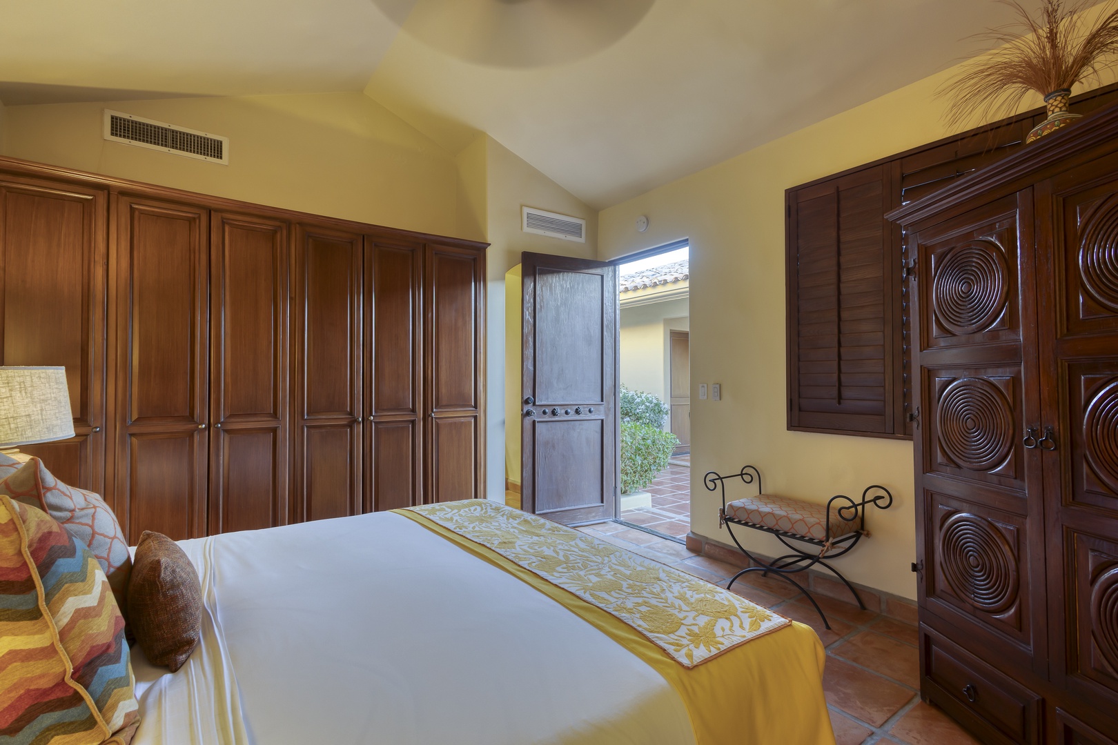 Relax in your elegant bedroom featuring rich wood cabinetry, warm colors, and a charming bench where you can unwind.