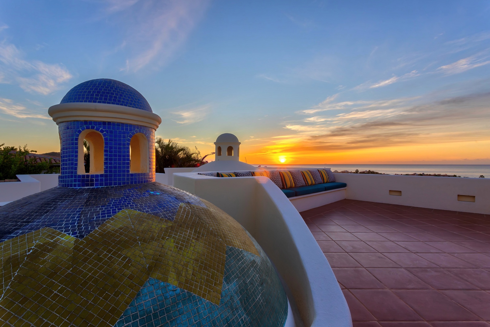 Stunning sunset views from a rooftop terrace featuring distinctive blue-tiled architecture and ocean vistas.