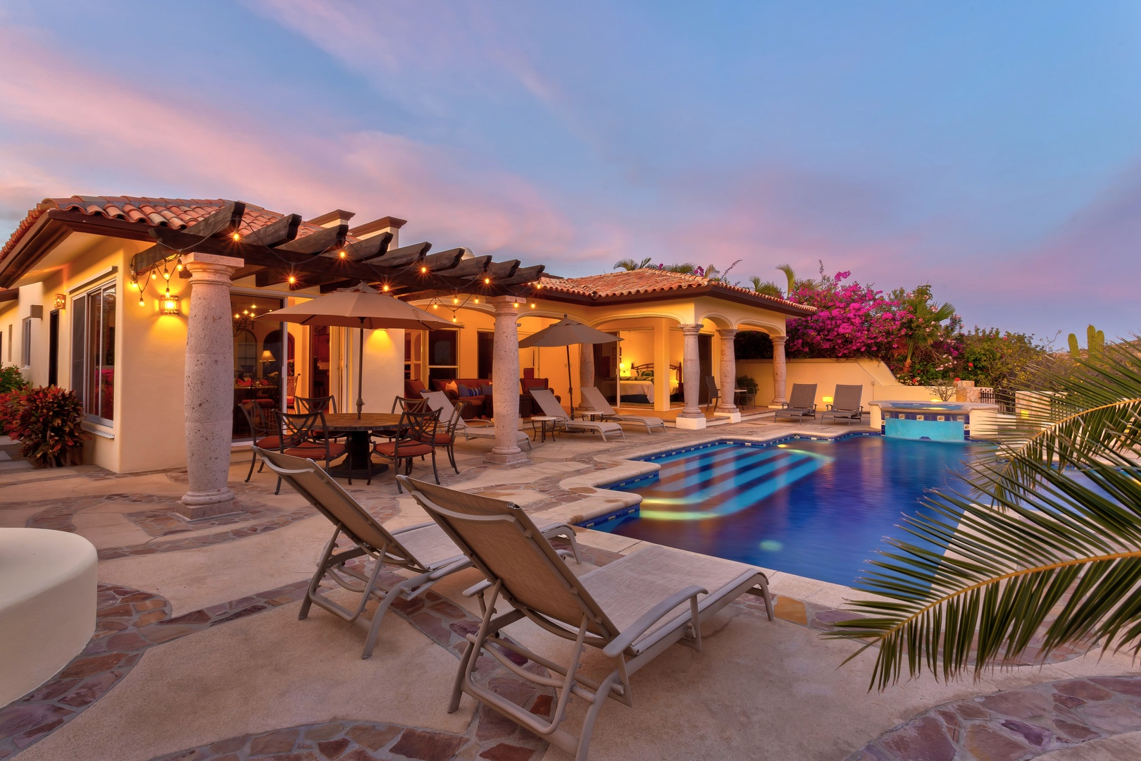 Stunning villa showcasing elegant architecture with covered terrace, pristine pool, and beautiful landscaping under a dramatic twilight sky.