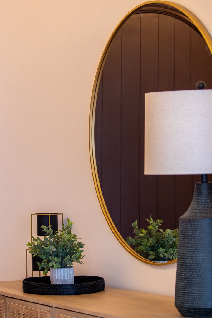 Thoughtful details create a warm, welcoming atmosphere in your space—notice the brass-framed mirror, modern lamp, and fresh greenery that add character to your retreat.