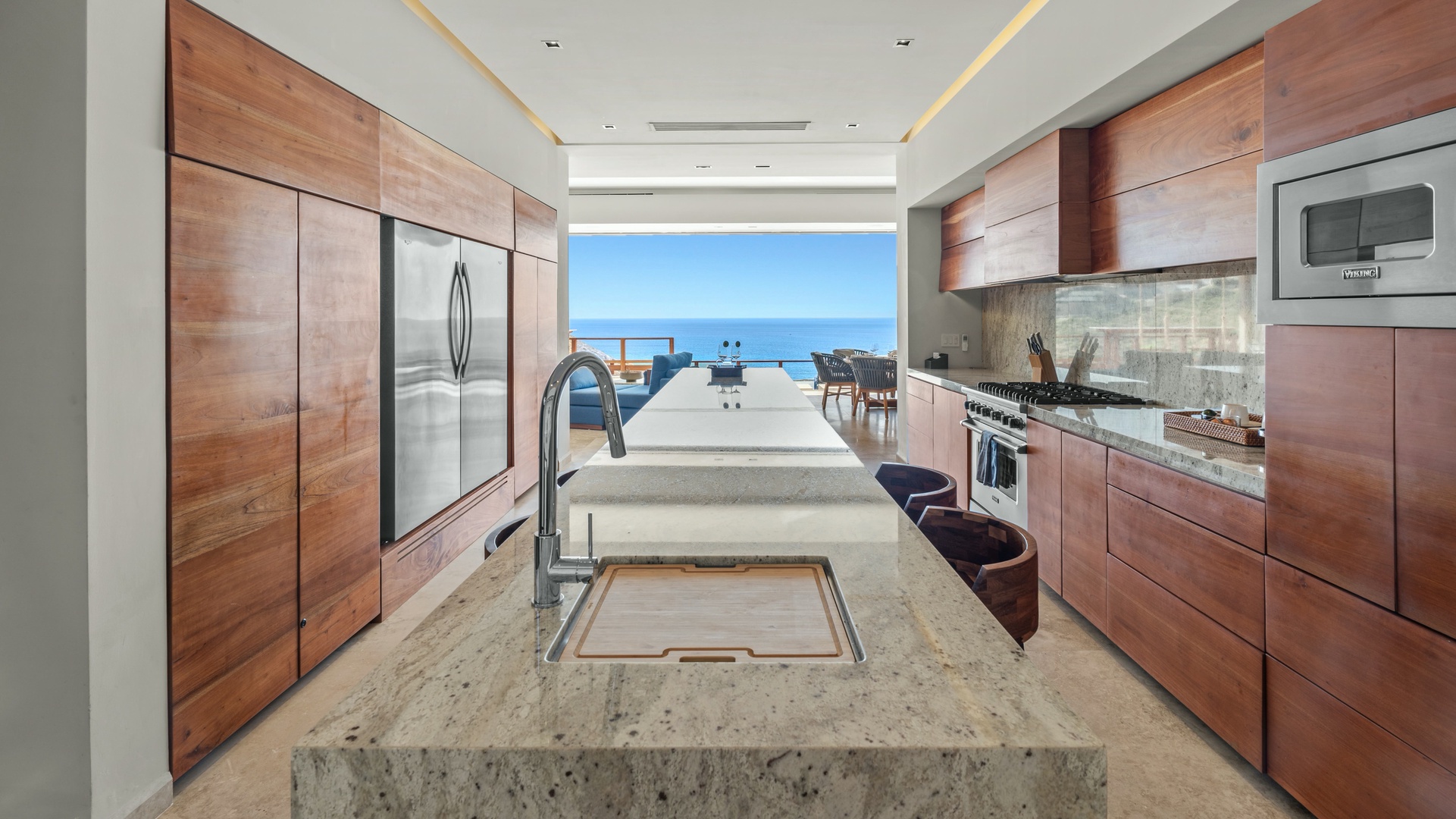 Picture yourself cooking in this modern kitchen with gleaming appliances and a stunning ocean view framing your mornings. Warm wood cabinetry meets sleek stone countertops where you'll enjoy meals with the sea breeze drifting in.