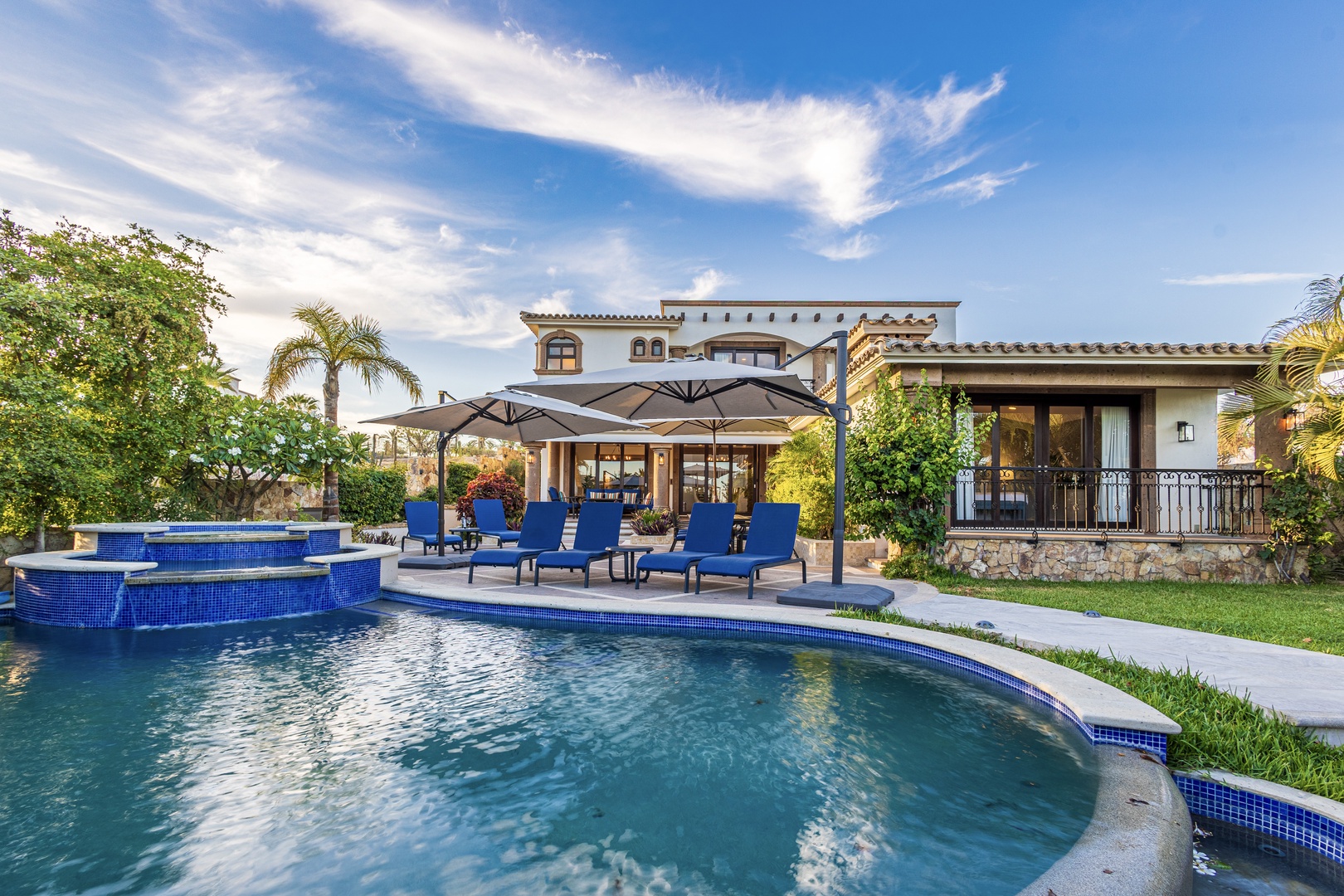 Elegant Spanish-style villa with sparkling pool, hot tub, and shaded lounging areas set amid lush tropical landscaping—an idyllic private retreat awaits.