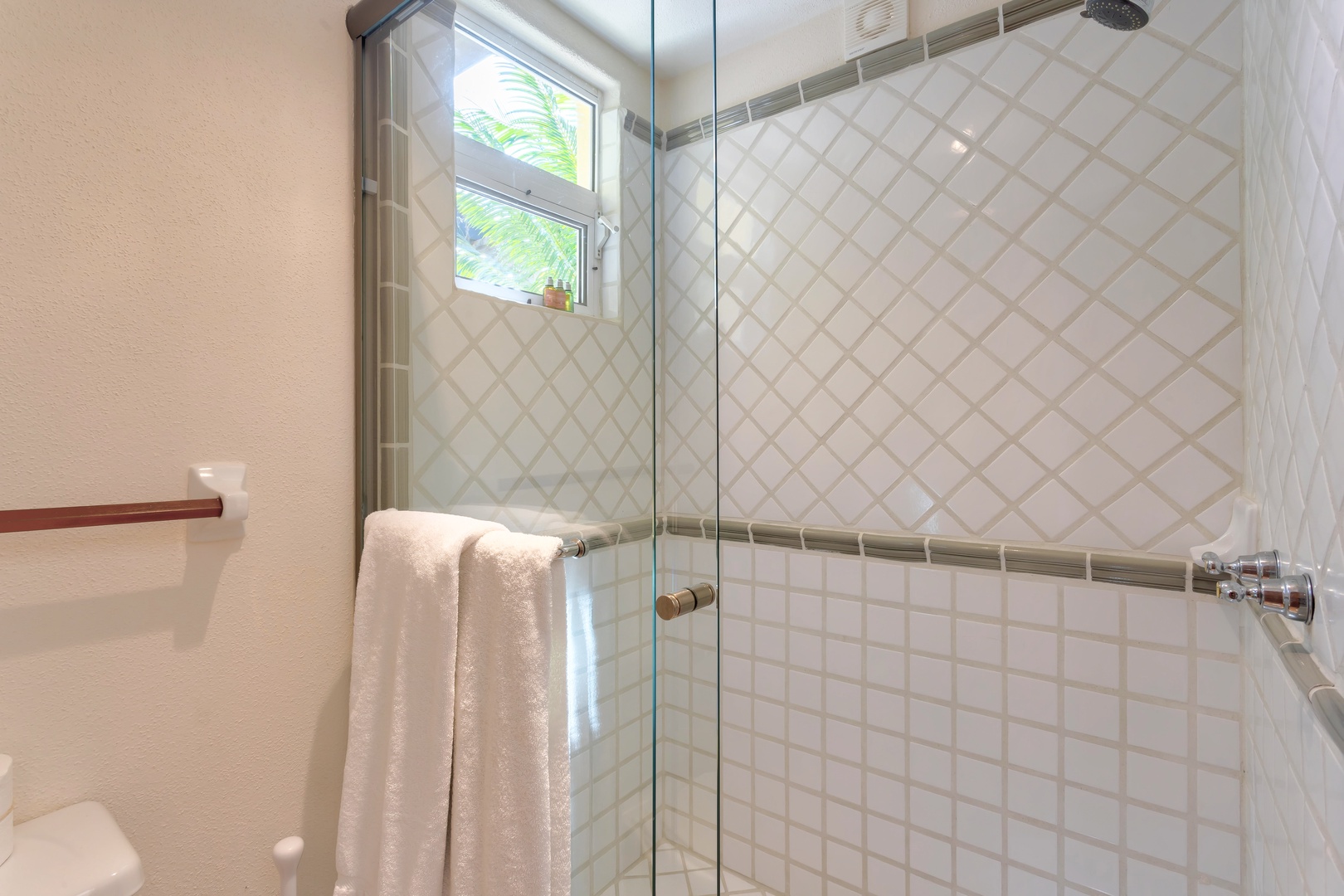 Step into your private glass-enclosed shower with beautiful white tiling and natural light streaming through the window for a refreshing start to your day.