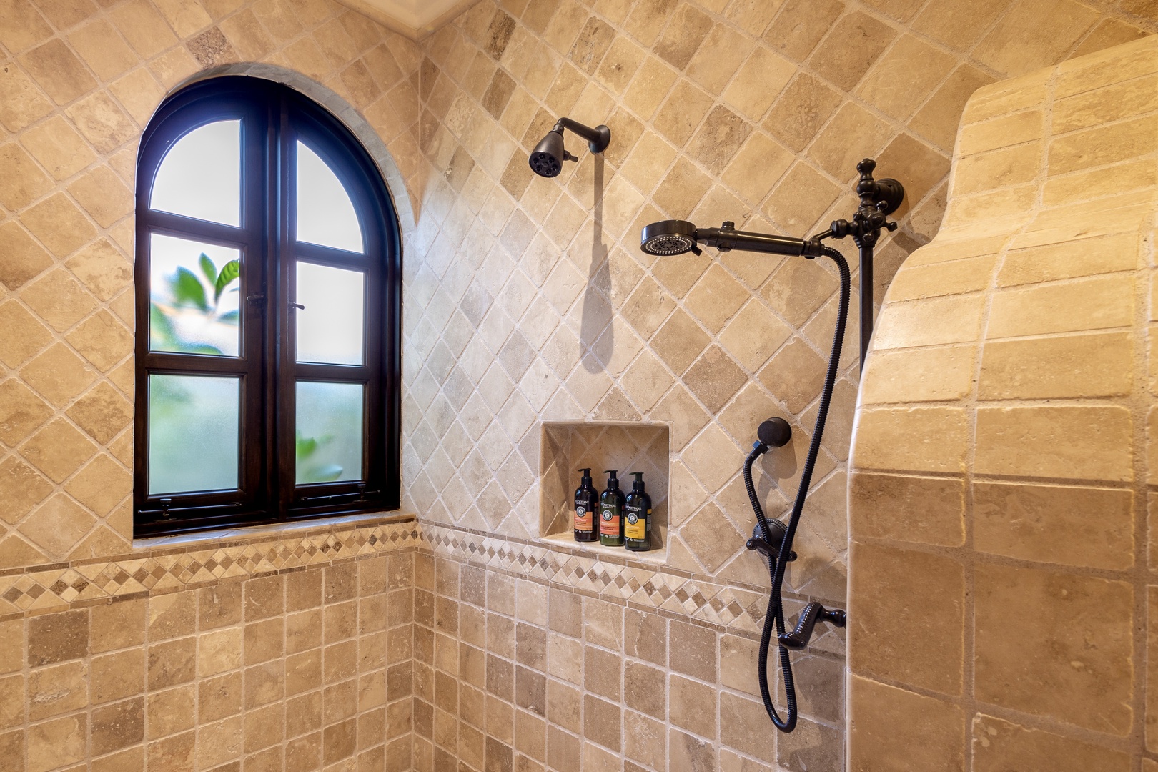Luxurious stone-tiled shower with dual heads and charming arched window—your private spa retreat awaits, with natural light and elegant fixtures to start your day refreshed.