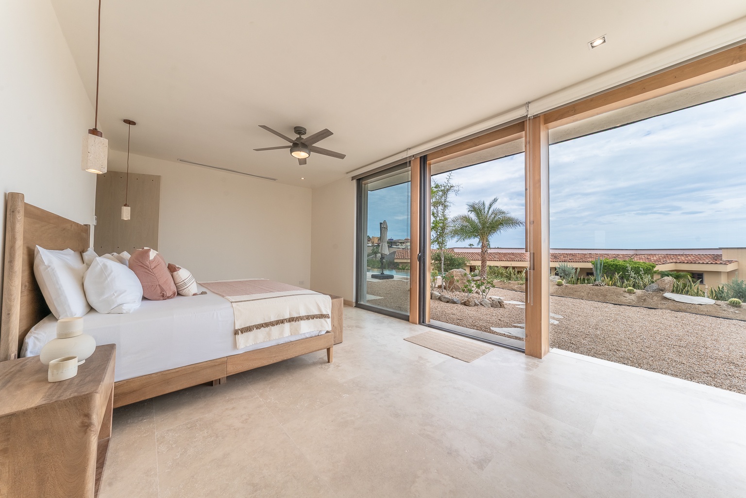 Drift off in your serene bedroom, where floor-to-ceiling glass doors frame desert views and palm-dotted landscapes, inviting natural light and tranquil vibes into your private sanctuary.