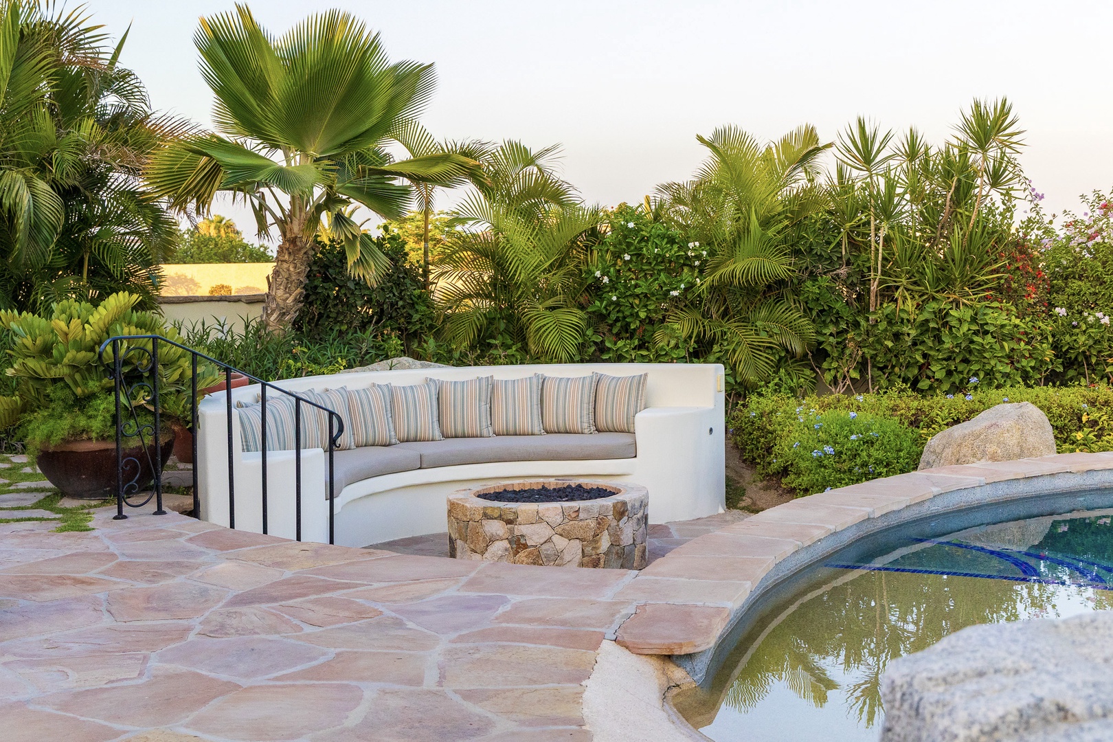 Lush tropical landscaping frames this serene outdoor retreat with built-in seating, fire pit, and sparkling pool—an idyllic spot for unwinding under the palms.