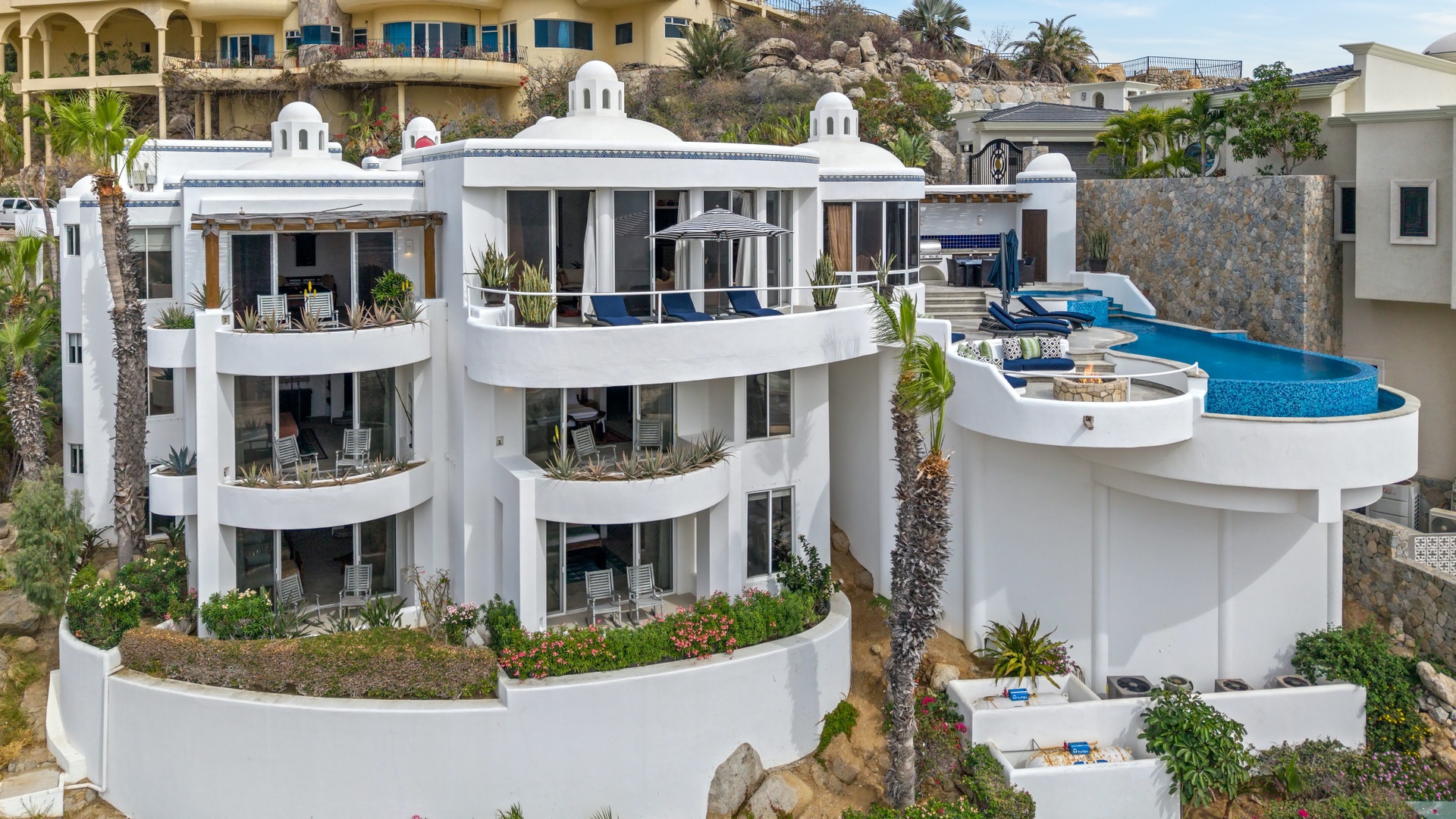 A stunning white villa with curved architecture features multiple terraces, private pool, and lush tropical landscaping.