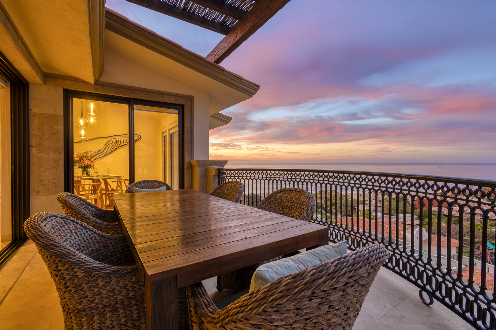 Stunning coastal sunset viewed from a private terrace in the area, with decorative ironwork railings and rooftops below, marking the arrival experience to this scenic location.