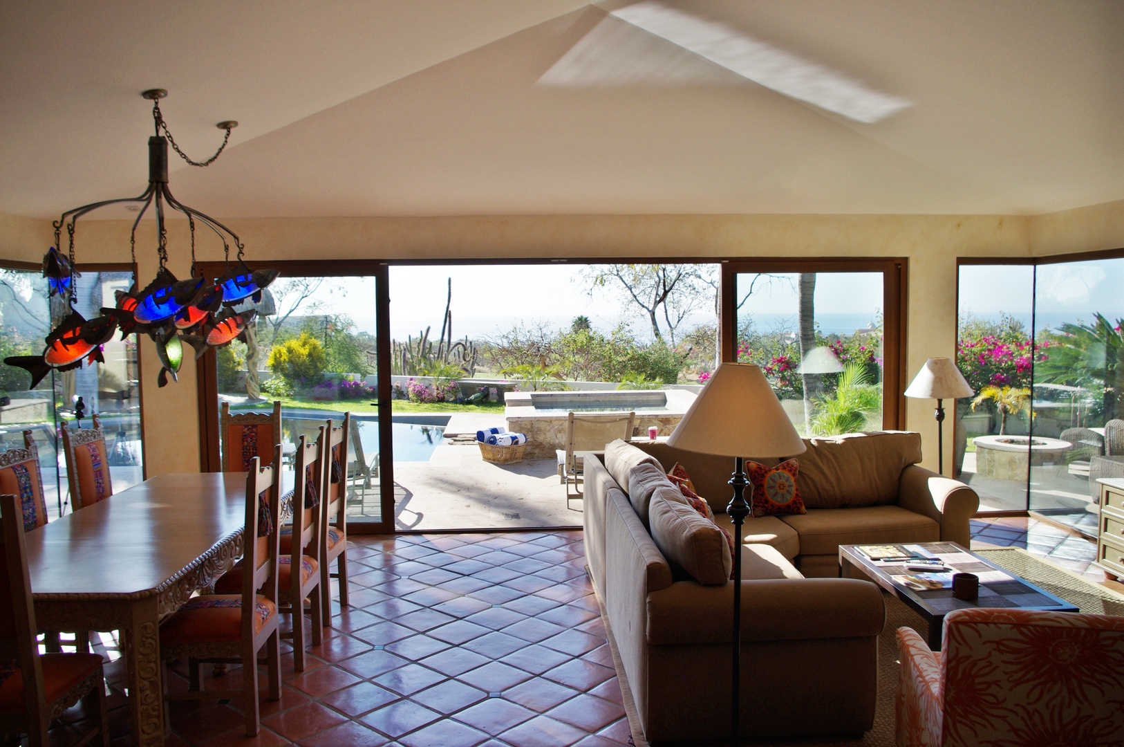 Sunlight streams through tall windows into your inviting living space, where cozy seating invites you to unwind while overlooking the sparkling pool and lush garden beyond.