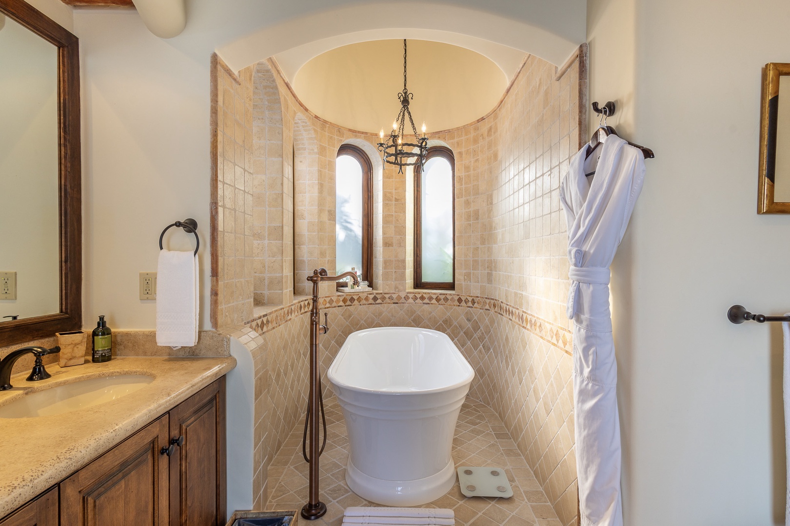 Step into your private spa-like retreat, where a luxurious freestanding soaking tub awaits beneath elegant arched windows and a glowing chandelier.