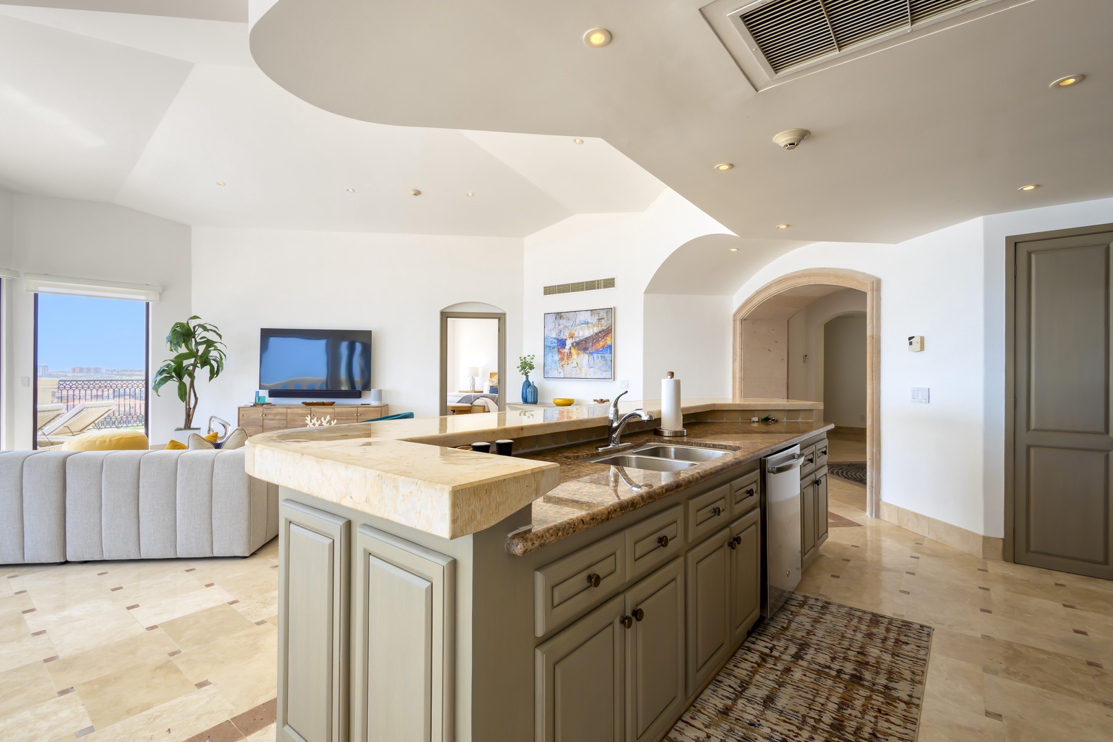 Step into your open-concept living space where natural light pours through elegant archways. The kitchen island becomes your gathering spot, while ocean views frame your perfect vacation backdrop.