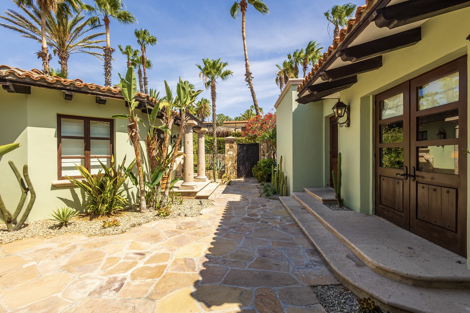Desert villa courtyard features stone pathways, tropical palms, and Spanish colonial architecture in a private oasis setting.