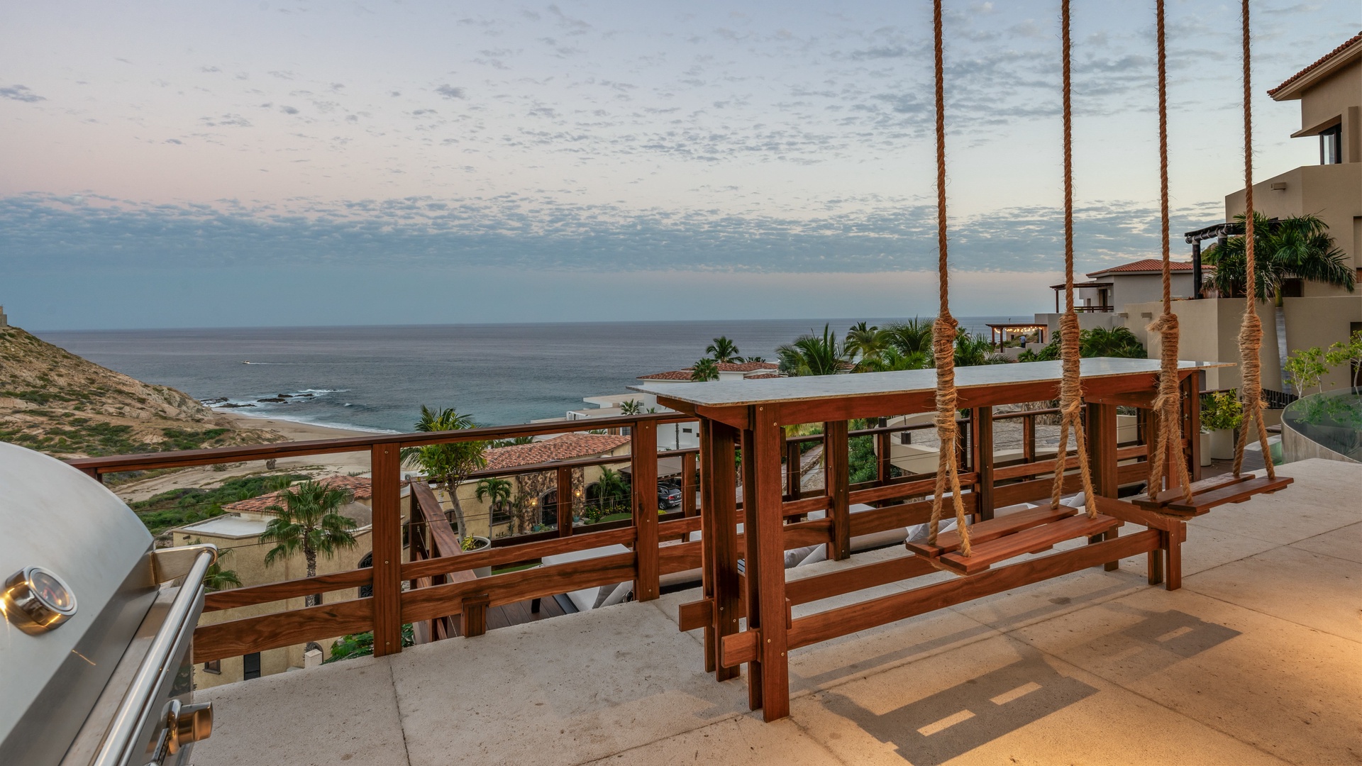 The property sits in a hillside coastal community with ocean views, palm trees, and nearby beach access, offering a tranquil retreat setting at dusk.
