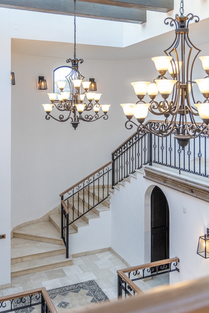 Soaring ceilings and ornate chandeliers welcome you into an elegant foyer where natural light spills across pristine tile floors and graceful curves of wrought iron stairways.