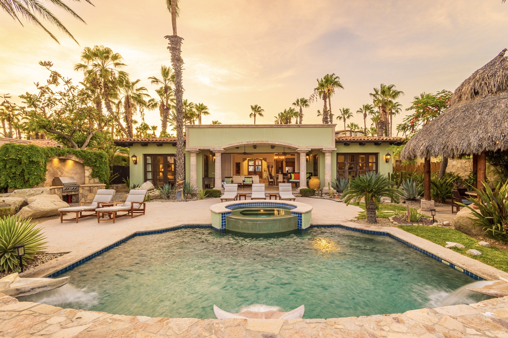 A stunning Spanish-style villa with a private pool and fountain awaits your arrival. Lush tropical gardens, palm trees, and a thatched palapa frame this serene outdoor retreat.
