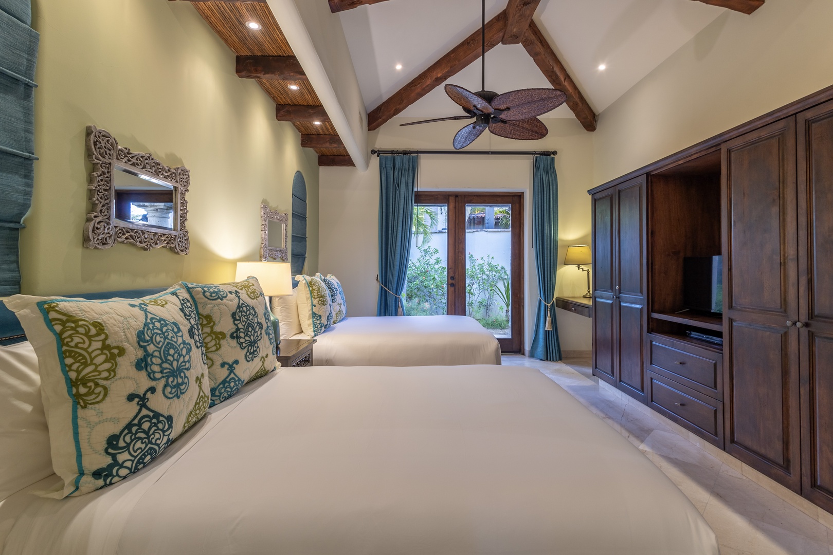 Rest easy in your serene retreat, featuring vaulted ceilings with exposed wood beams, crisp linens, and elegant furnishings. French doors open to a private garden view, inviting gentle breezes and natural light into your tranquil sanctuary.