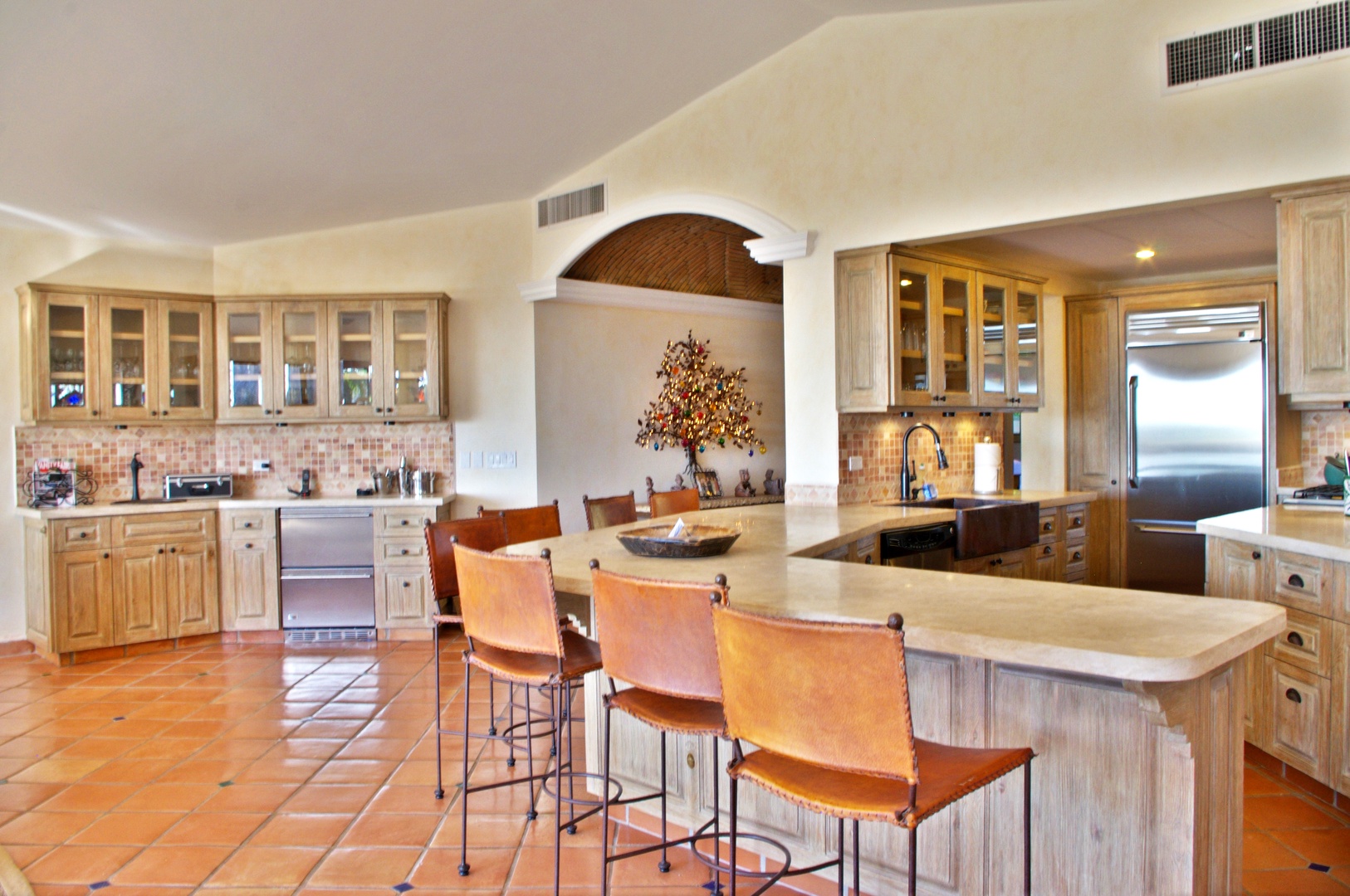 Spacious gourmet kitchen with warm terracotta floors, elegant arched alcove, and generous island seating where you can enjoy morning coffee or casual meals in Southwest-inspired comfort.