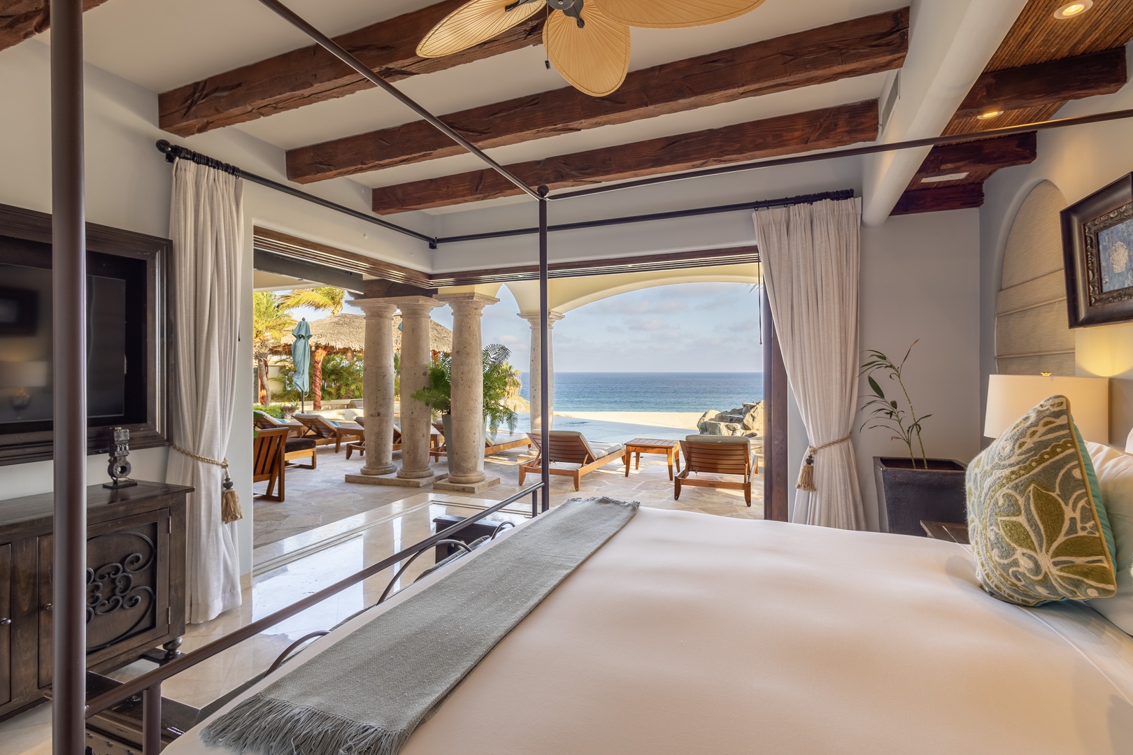 Your private sanctuary opens to a breathtaking beach vista framed by elegant columns, where you can unwind on the plush bed or step out to lounge under the tropical sky with the soothing sound of waves nearby.