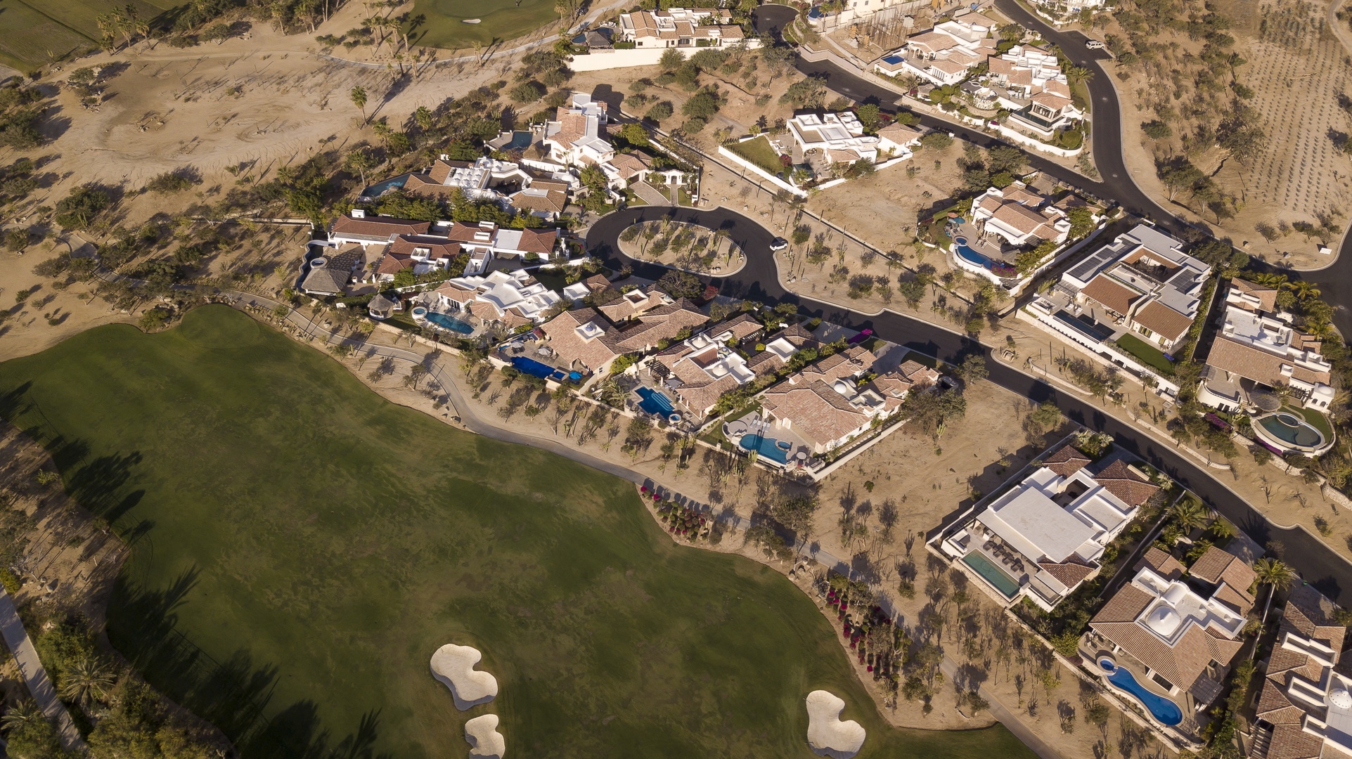 Aerial view of an upscale residential community featuring Mediterranean-style homes with pools nestled around manicured golf course fairways.