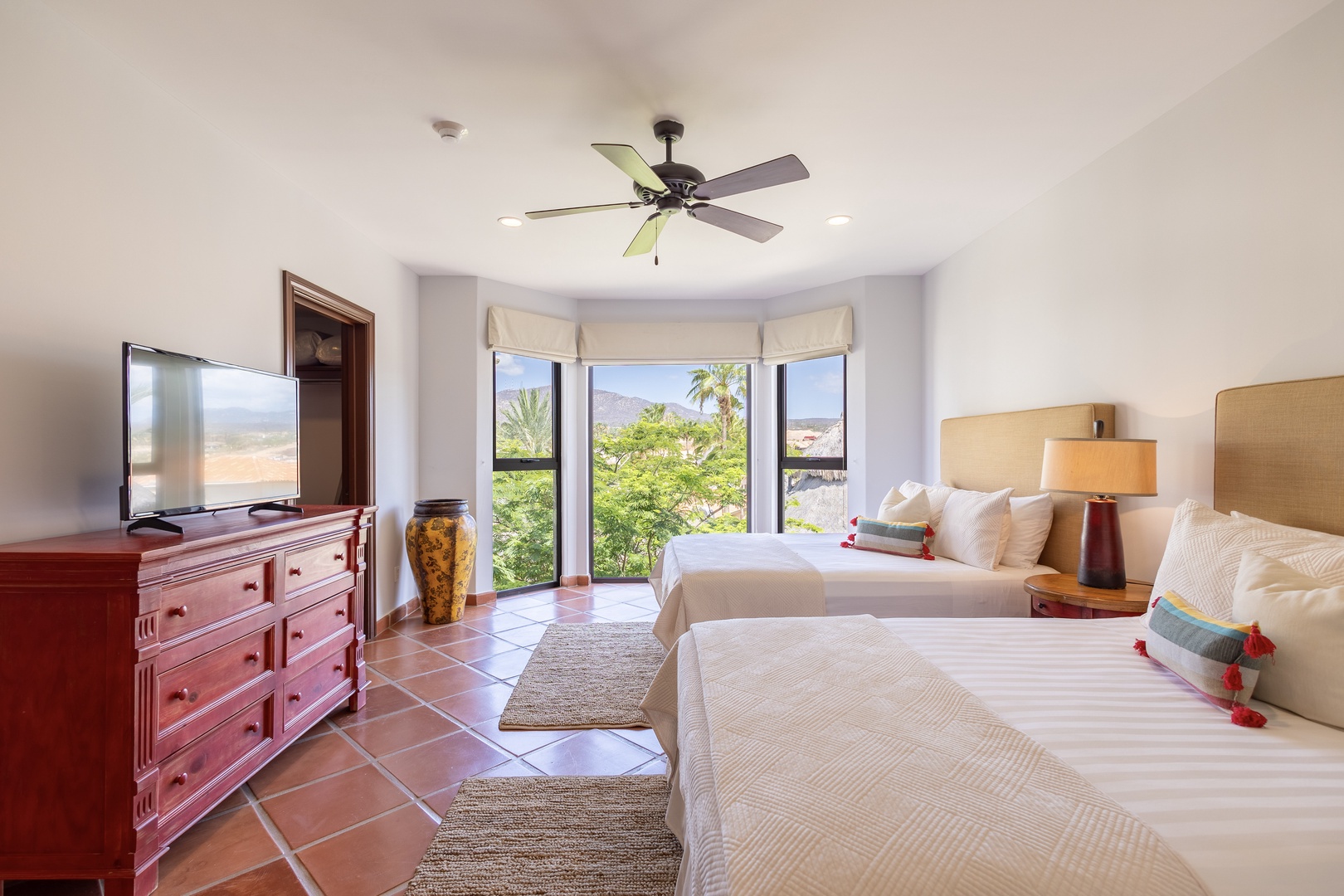Wake up to serene mountain views framed by lush greenery from your cozy retreat. Two inviting beds await, dressed in crisp linens and cheerful accents, while gentle breezes from your ceiling fan and terracotta floors keep the space cool and relaxed.