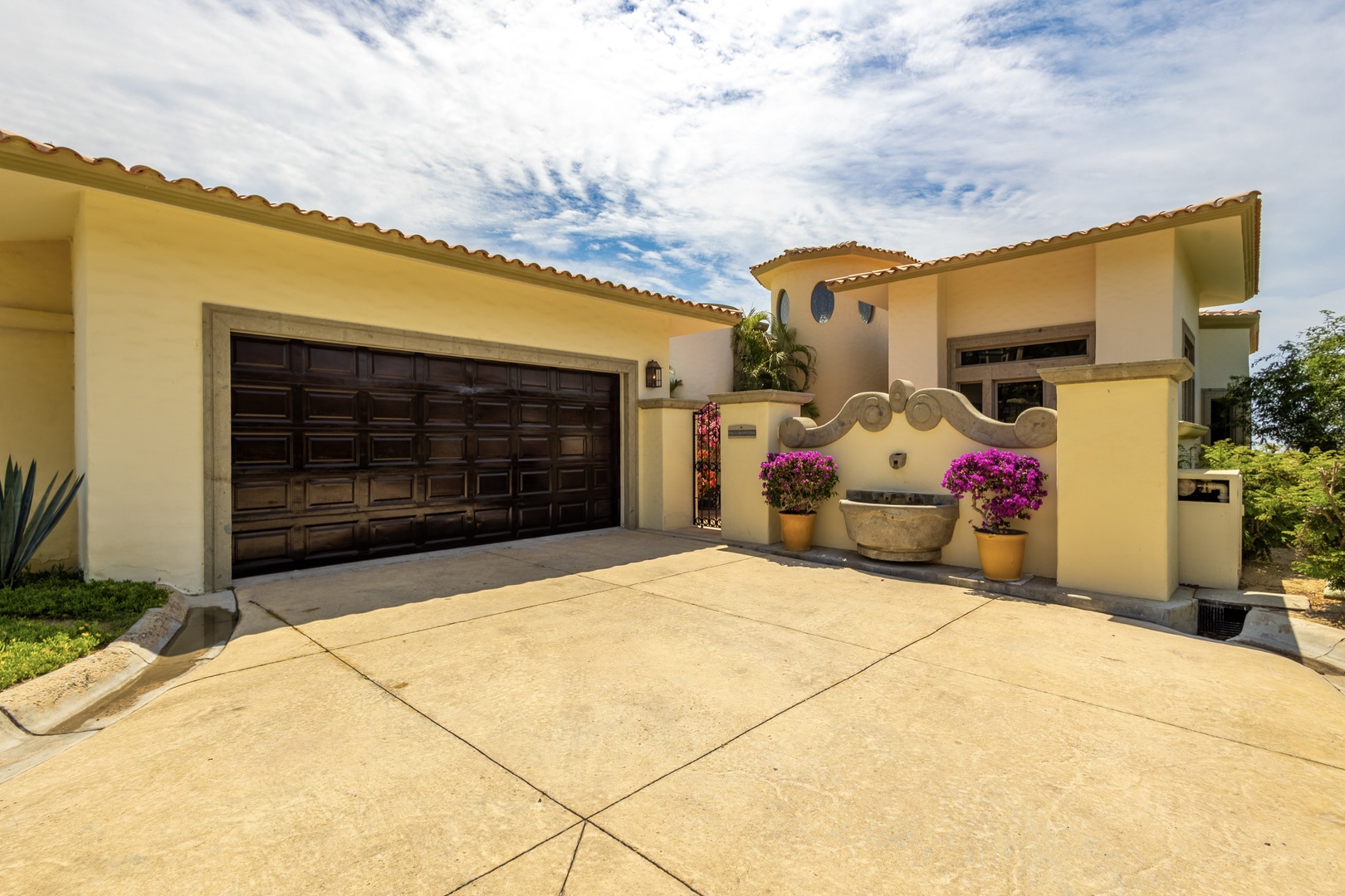 Charming Mediterranean-style villa welcomes guests with warm yellow stucco walls, terracotta tile roof, and vibrant purple bougainvillea framing the entrance courtyard.
