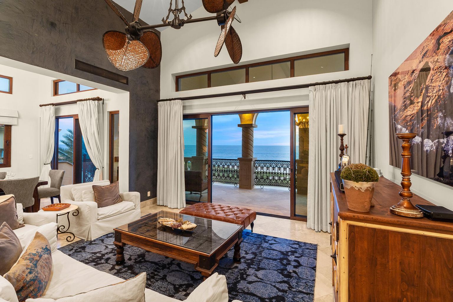 Step into your elegant living room where soaring ceilings and warm tropical touches meet stunning ocean views. Unwind on plush seating as the sound of waves drifts through open doors.