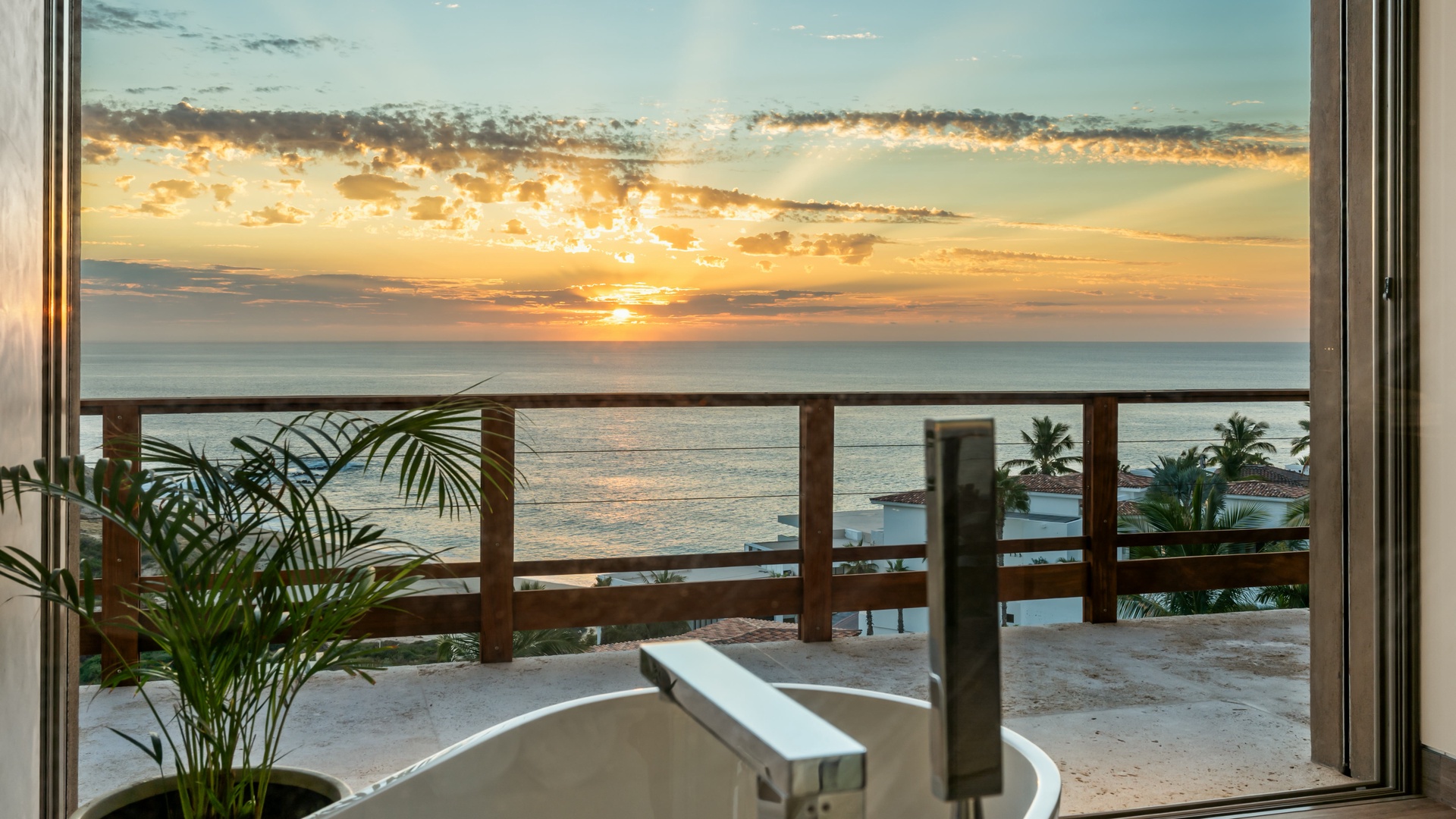 Stunning beachfront sunset view from the balcony with ocean horizon, pool, and palm trees—a tranquil backdrop to unwind after a day of adventure.