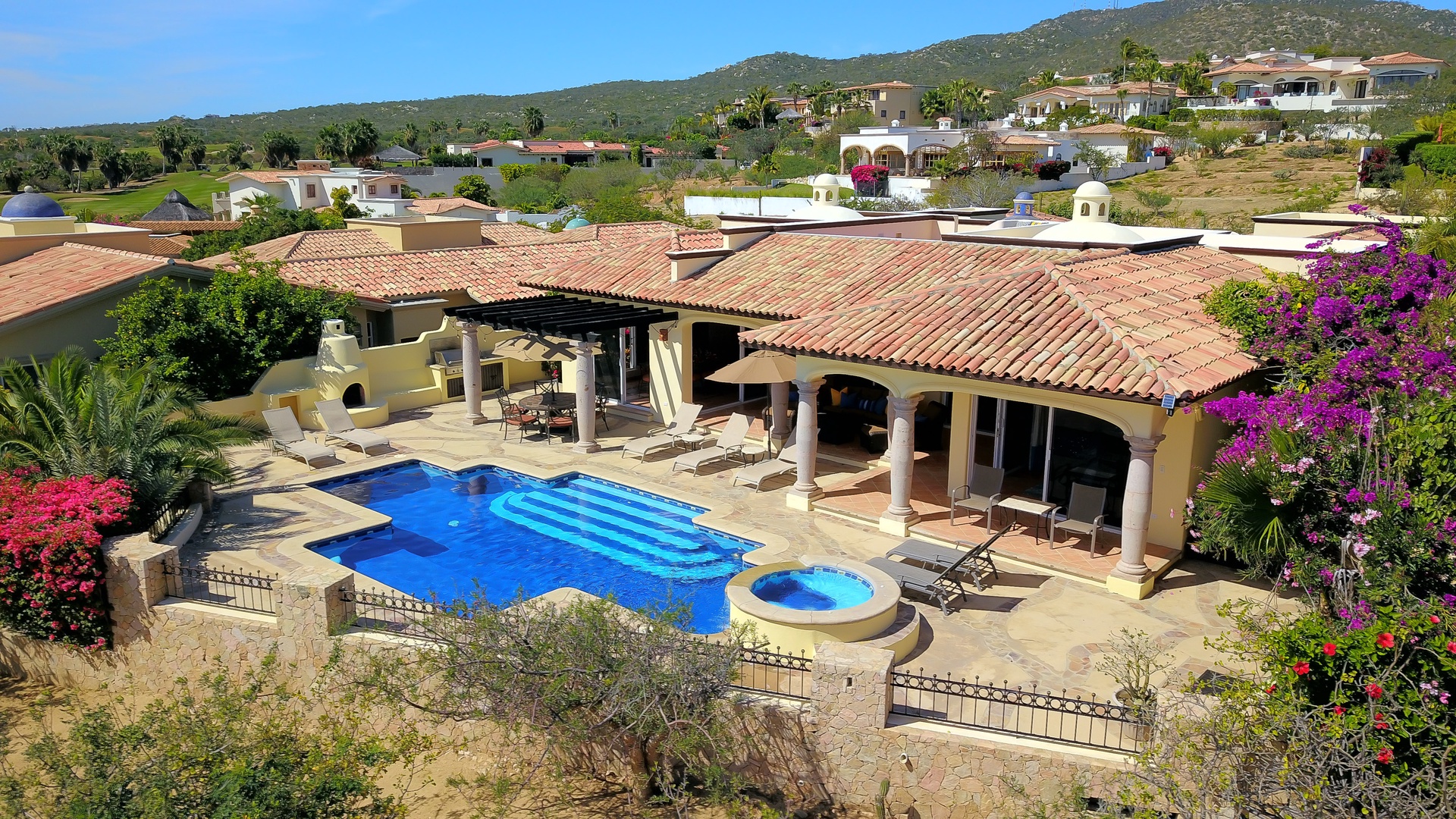 Elevated villa with private pool and hot tub, surrounded by vibrant bougainvillea in a hillside community setting.