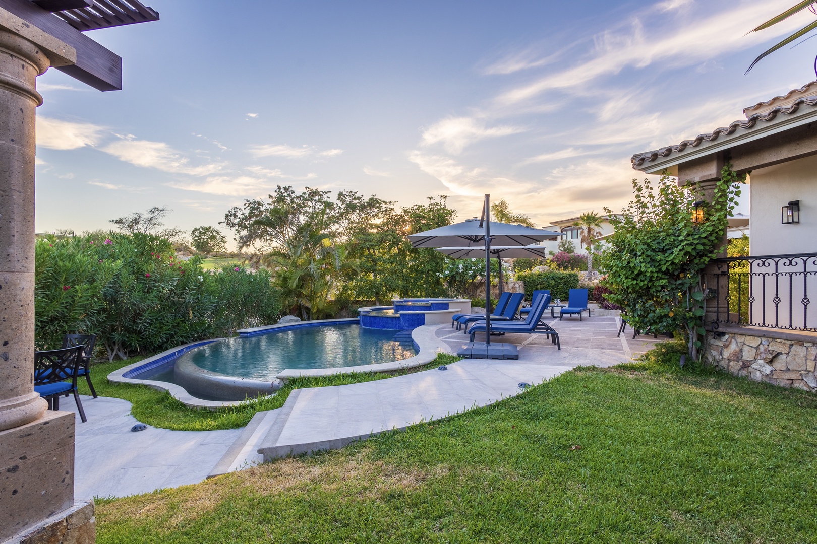 Private backyard oasis featuring a beautifully landscaped pool area, surrounded by lush greenery and outdoor seating perfect for peaceful evenings under open skies.
