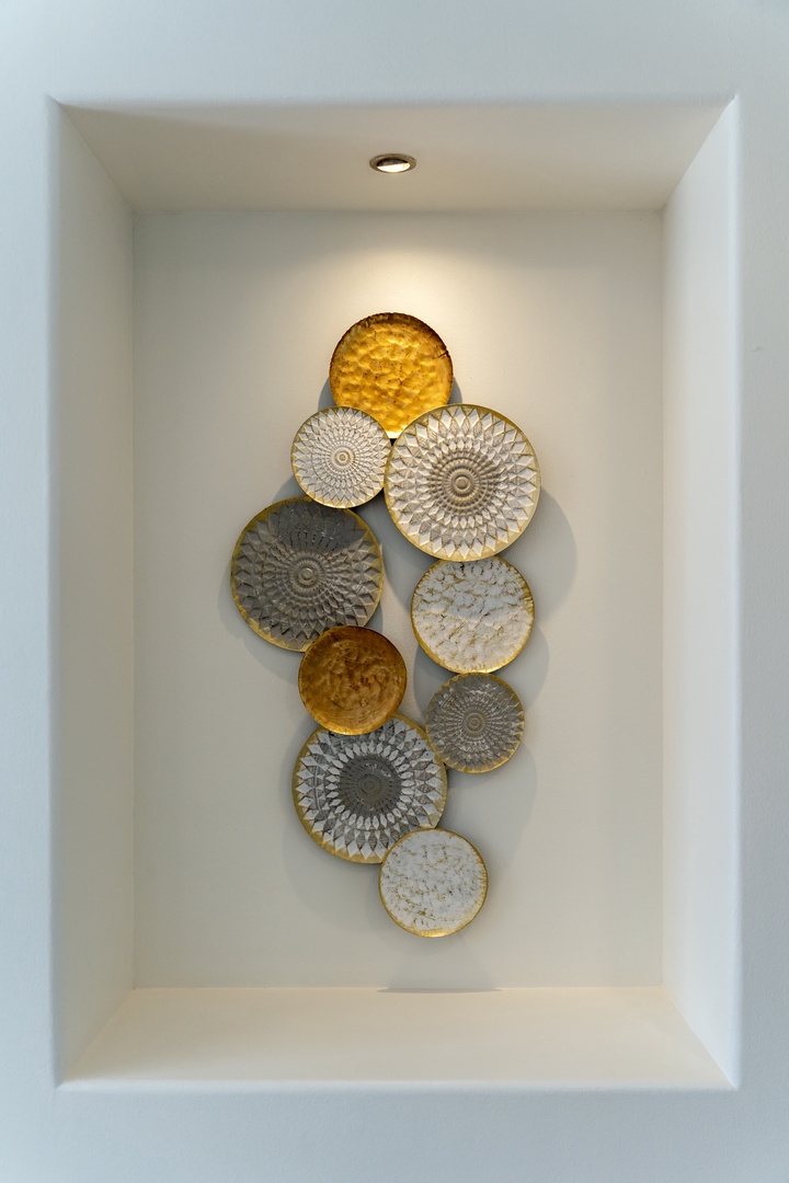 Admire the elegant wall niche featuring beautiful decorative plates in warm golds and soft neutrals, perfectly illuminated to create a welcoming artistic focal point.