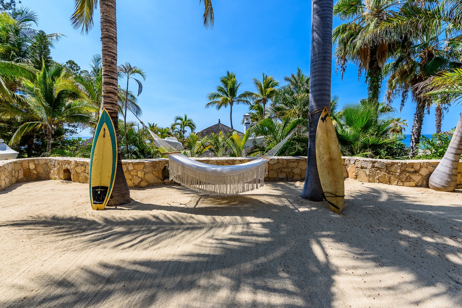Swing gently in your private hammock beneath swaying palms, with surfboards ready for ocean adventures and tropical views all around.