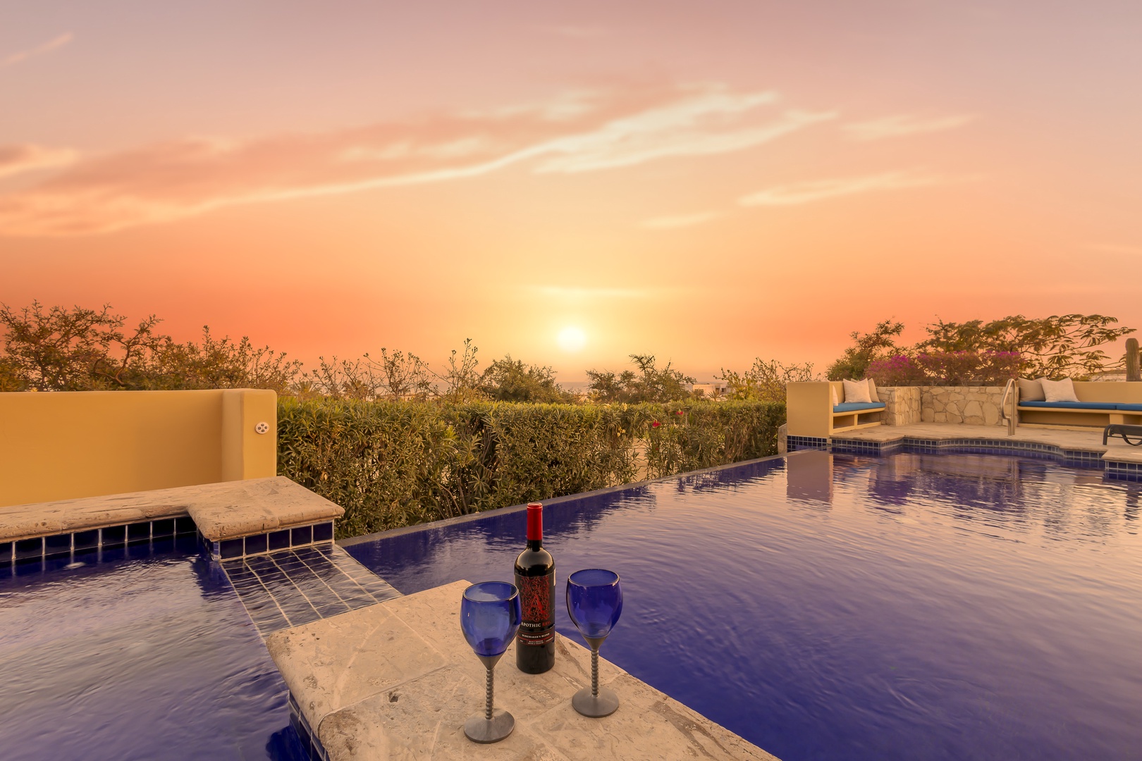 Stunning sunset paints the sky in warm hues over this beautiful swimming pool area with elegant seating and tropical landscaping.