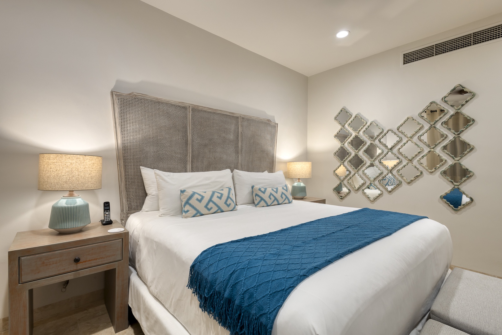 Sink into crisp white linens beneath a sculptural headboard, where soft bedside lamps and artistic mirrors create your serene coastal retreat.