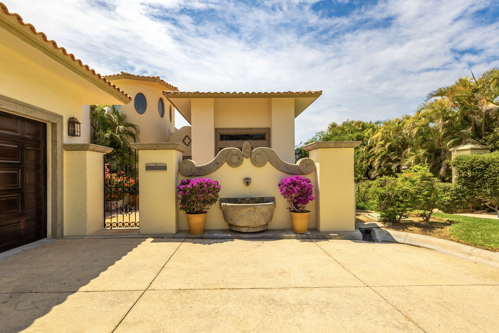 Mediterranean-style entrance with decorative fountain, terra cotta tiles, and lush tropical landscaping creates a welcoming first impression for your stay.