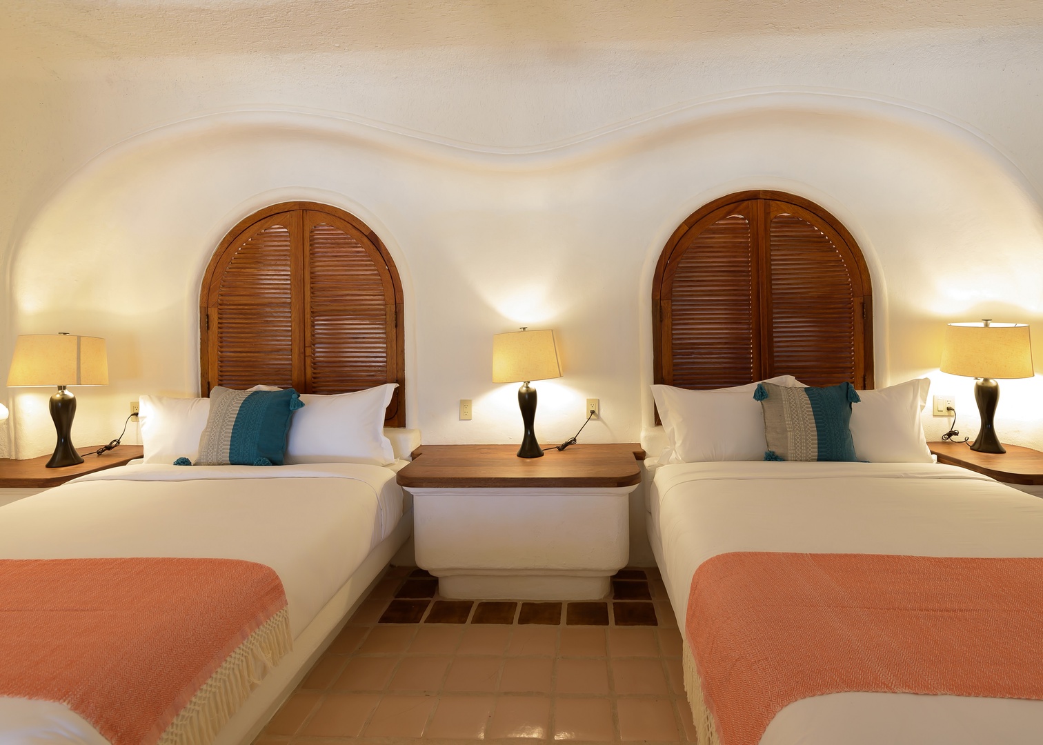 Relax in your beautifully appointed bedroom featuring two plush beds, elegant arched wooden headboards, and warm lighting that creates a soothing, restful atmosphere perfect for unwinding after your adventures.