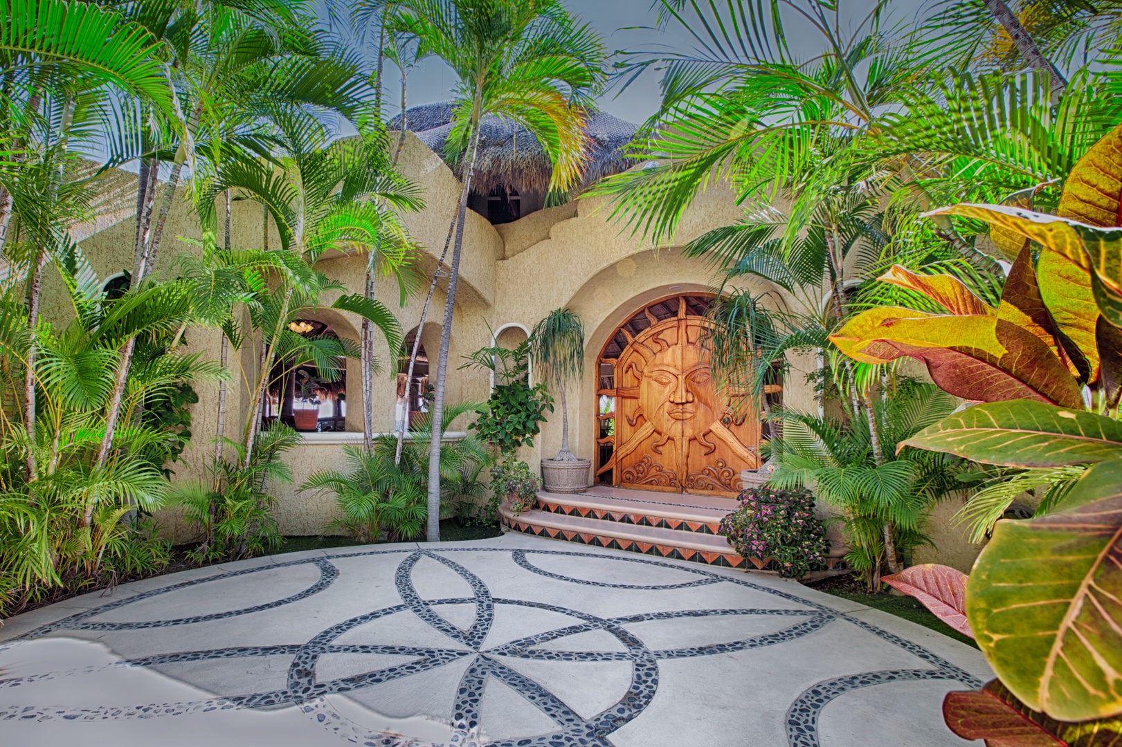 This stunning property entrance features intricate stonework and lush tropical landscaping, creating an impressive arrival experience.