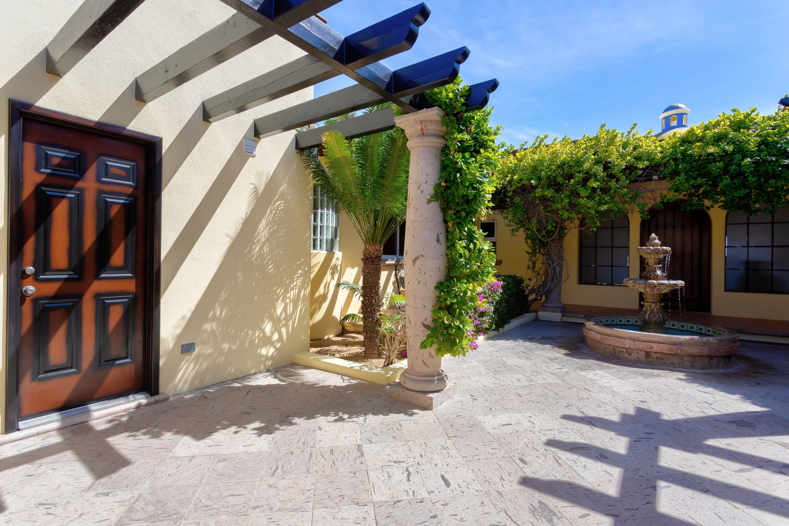Charming colonial-style courtyard entrance with traditional fountain and lush tropical landscaping under blue skies.