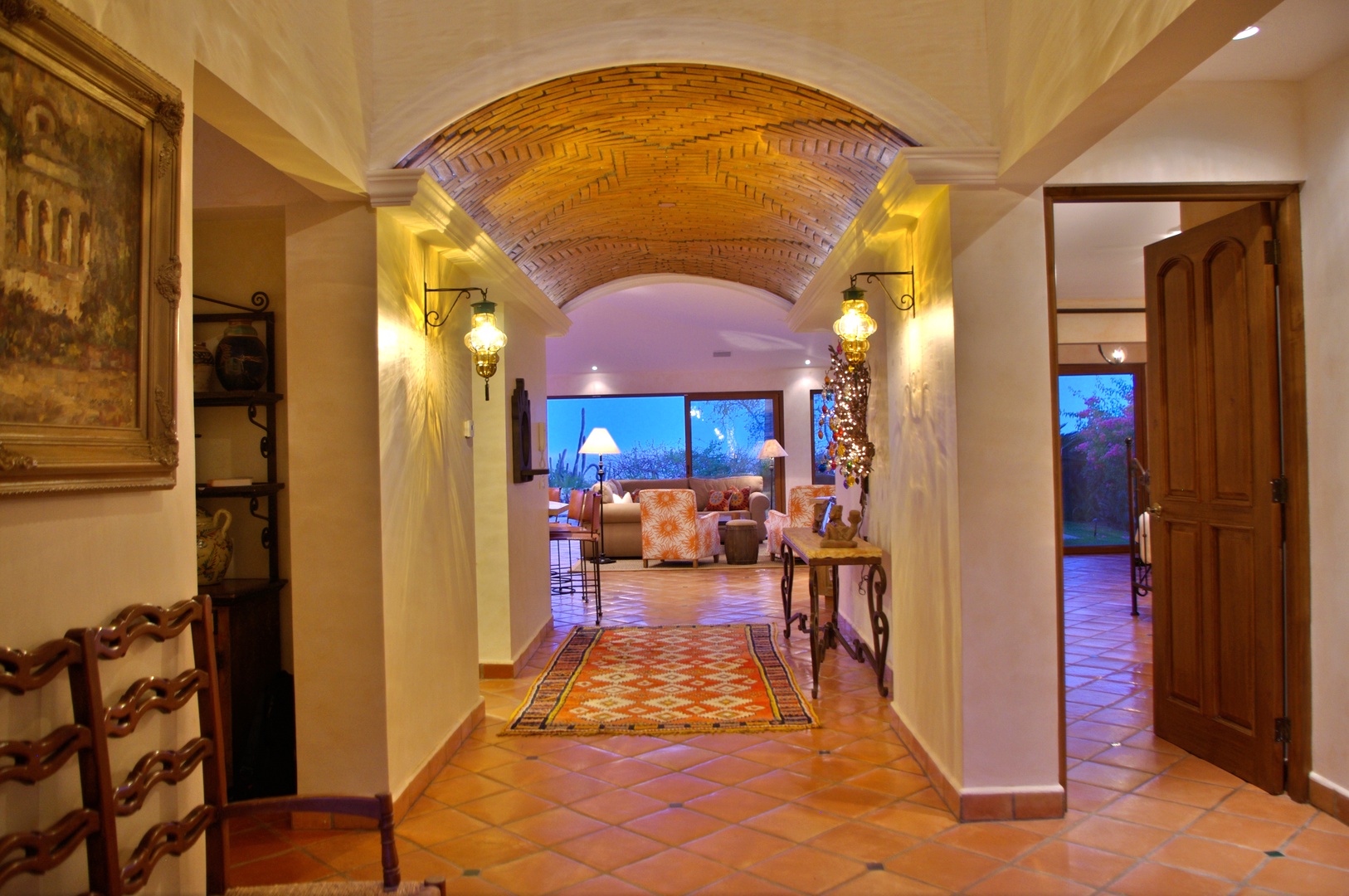 Step through a stunning brick archway into this inviting space where warm terracotta tiles and elegant wall sconces guide you toward a cozy lounge area that awaits your arrival.