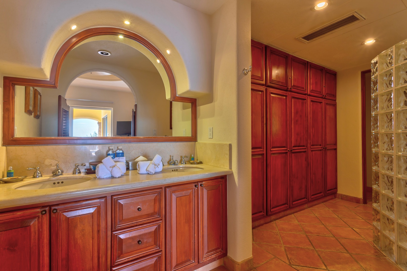 Step into your elegant bathroom featuring warm wood cabinetry, dual vanities, and luxurious amenities thoughtfully arranged for your comfort.